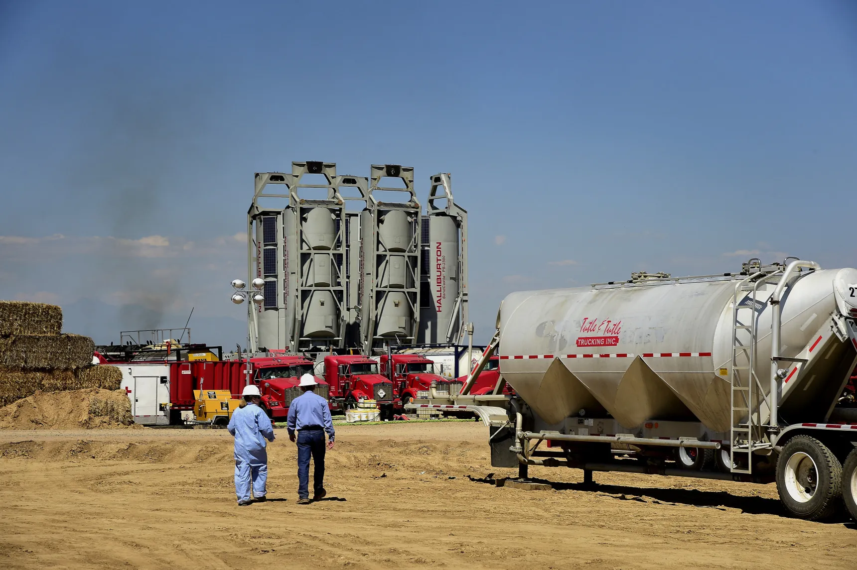 Workers walk towards Halliburton Co. "sand castles" at an Anadarko Petroleum Corp. hydraulic fracturing (fracking) site north of Dacono, Colorado, U.S., on Tuesday, Aug. 12, 2014.