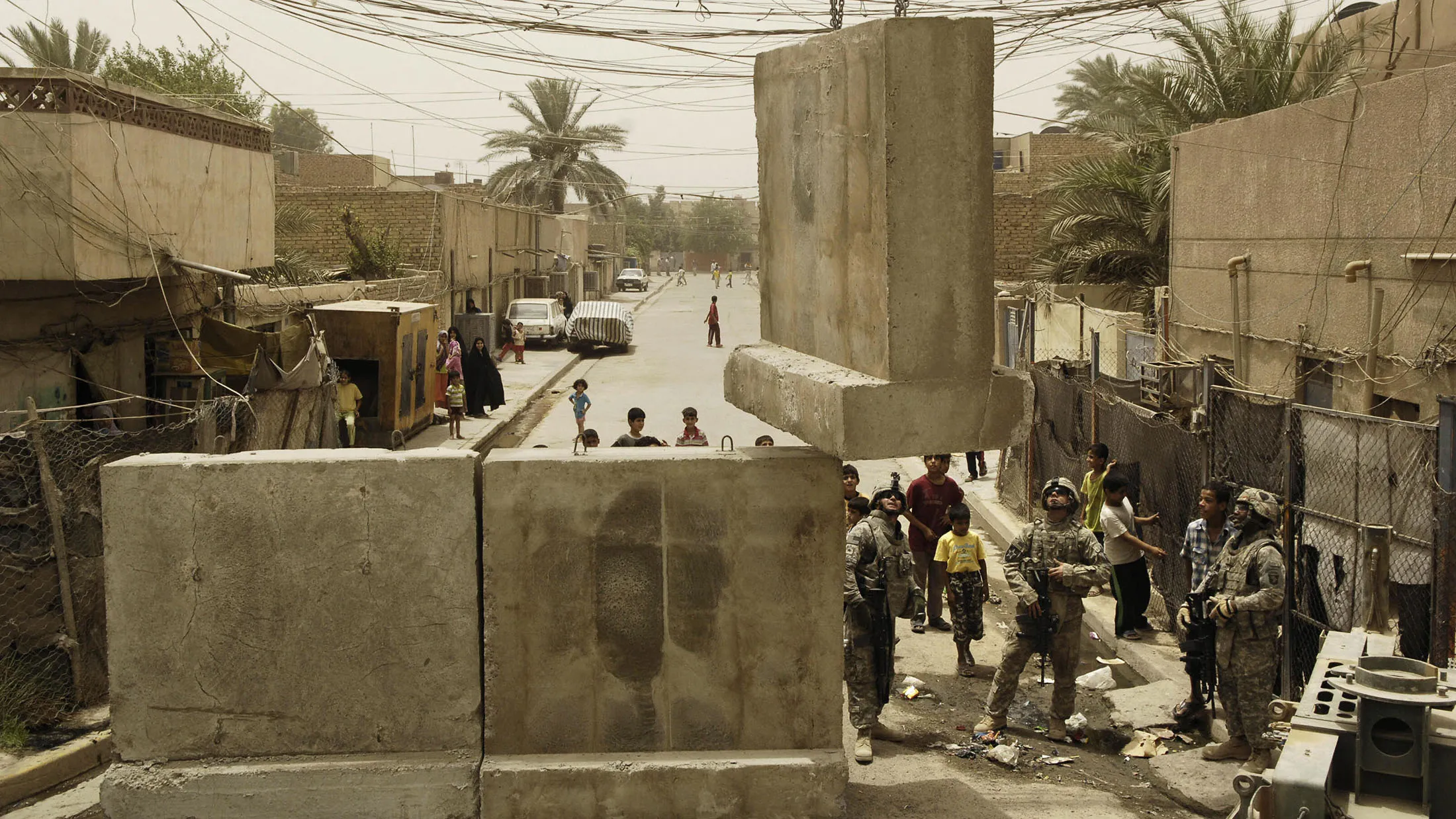 In this photo provided by the U.S. military, U.S. Army soldiers (bottom right) guide a concrete barrier into position as a crane lowers it to a street opening near the Joint Security Station in Shula, Baghdad, on June 8, 2008.
