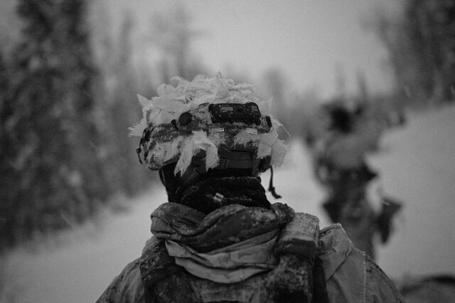 A soldier with the 11th Airborne Division wears a helmet fitted with white camouflage scrim to blend into snow-covered terrain.