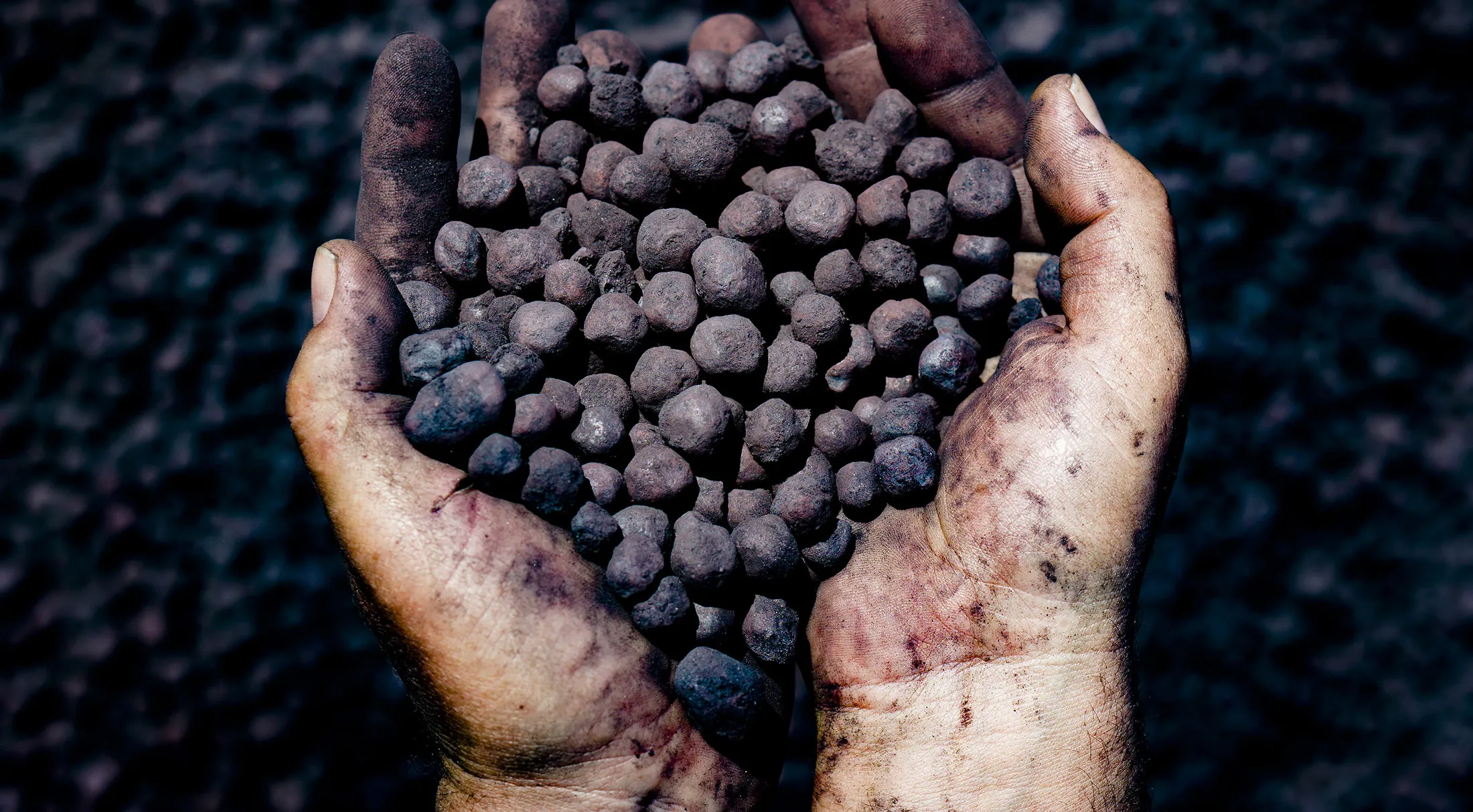 A worker holds a handful of iron ore pellets

