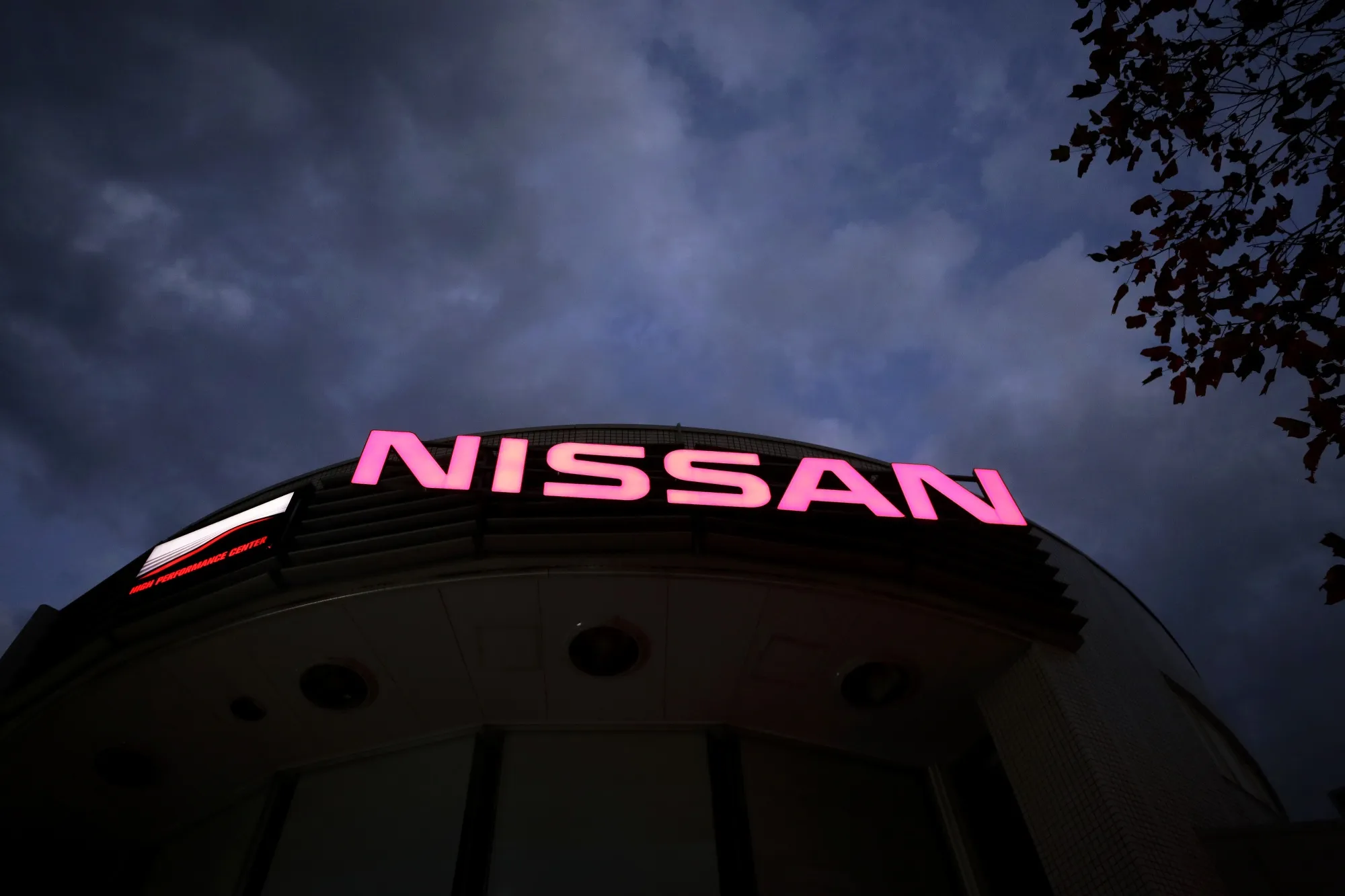 Illuminated signage atop a Nissan Motor dealership at dusk.