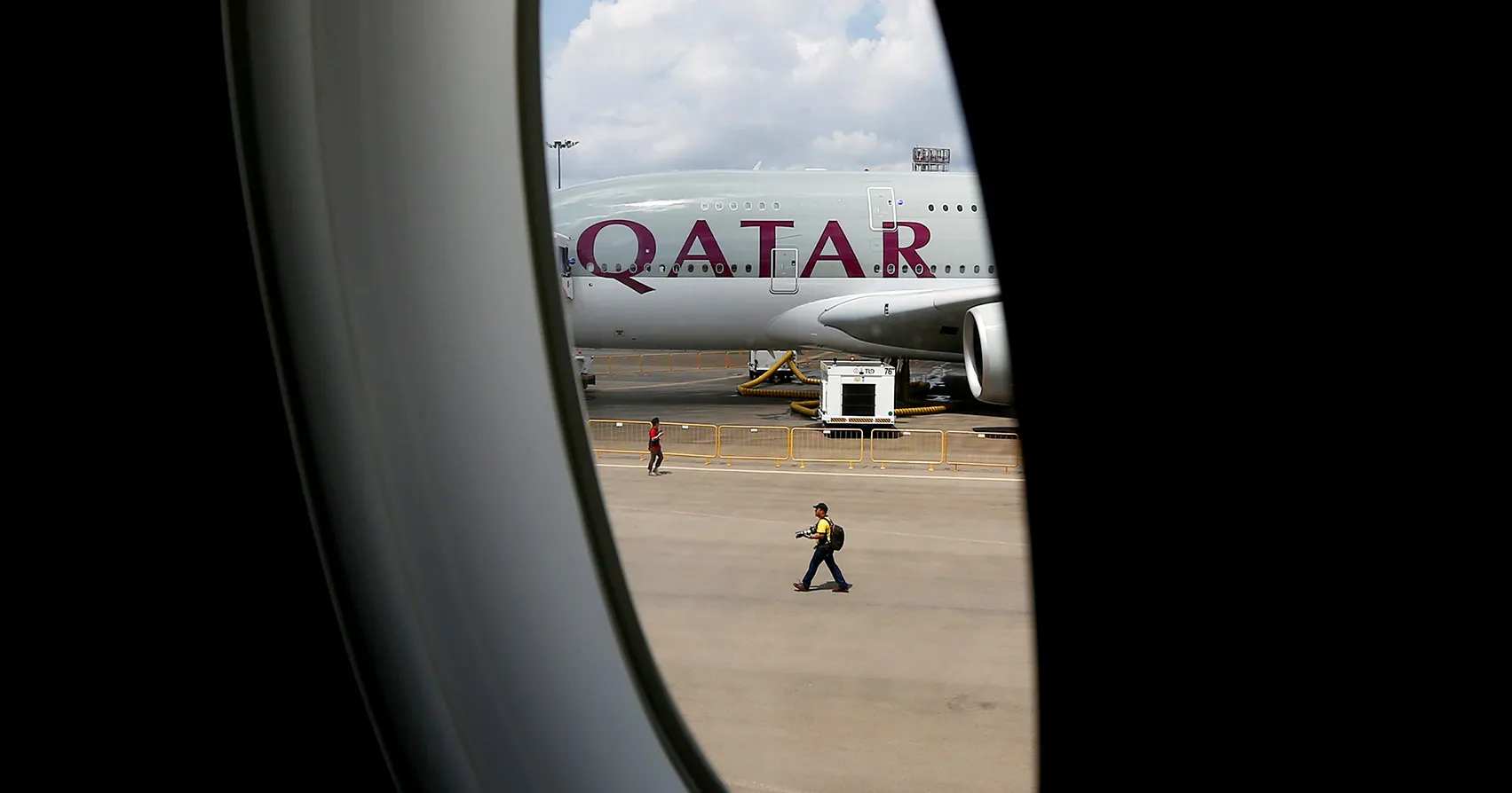 A Qatar Airways Ltd. Airbus A380 aircraft sits on the tarmac seen through a window of an Airbus A350 XWB aircraft operated by the airline at the Singapore Airshow held at the Changi Exhibition Centre in Singapore, on Tuesday, Feb. 16, 2016. Qatar Airways, the second-biggest Gulf carrier, will seek compensation for delays in delivery of its Airbus Group SE A320neo aircraft, Chief Executive Officer Akbar Al Baker said.
