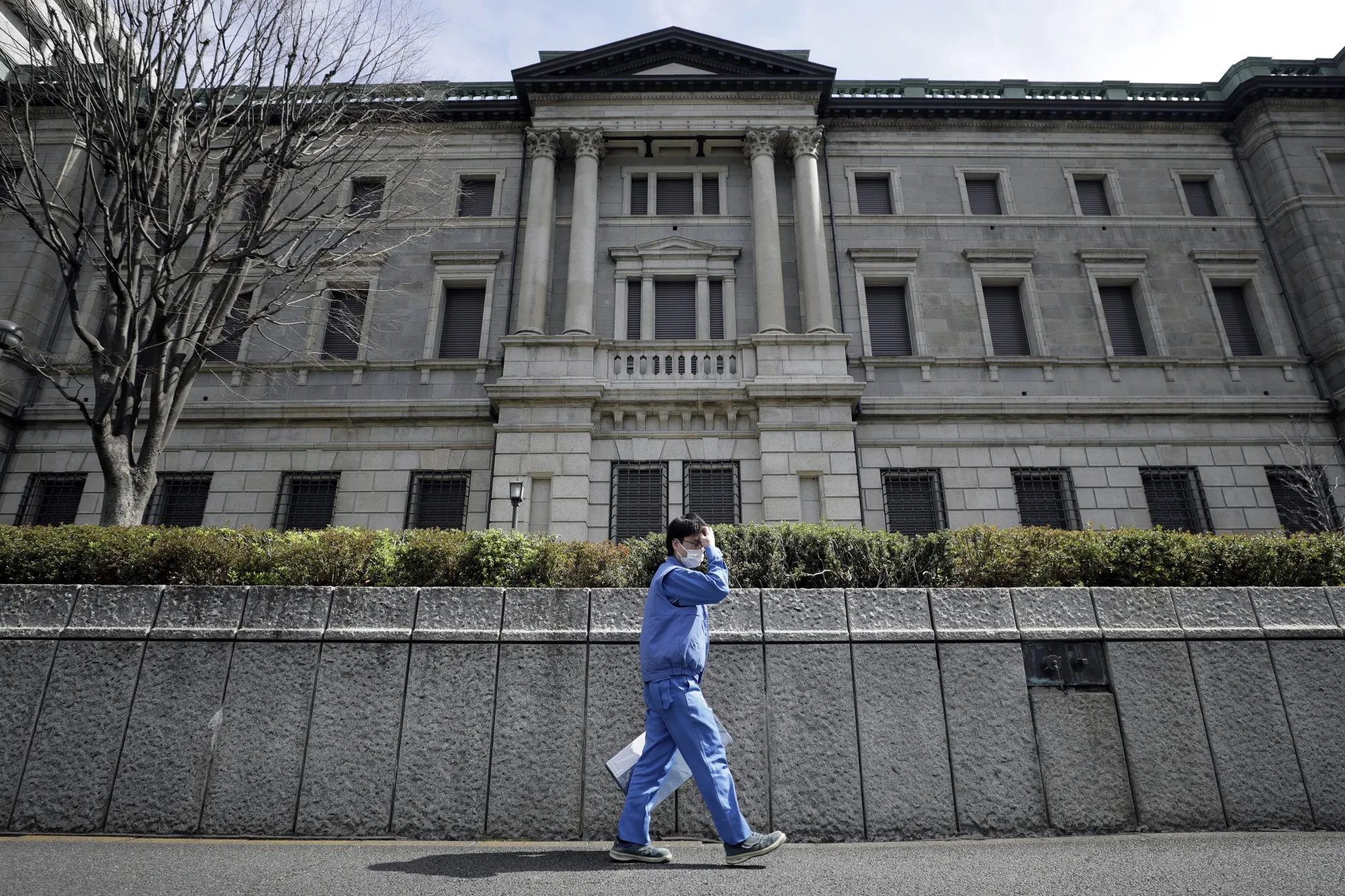 A pedestrian wearing a protective mask walks past the Bank of Japan&nbsp;headquarters in Tokyo.