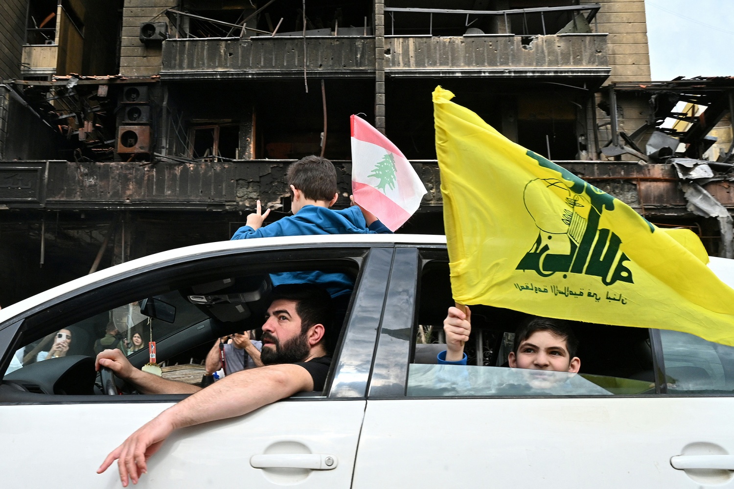 Boys wave Lebanese and Hezbollah flags while going past a heavily damaged building as displaced people return to their neighborhood in Beirut's southern suburbs on April 17.