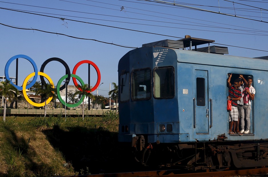 Passengers hang on the doors of a train as it passes the Olympic rings placed at the Madureira Park ahead the Rio 2016 Olympic Games, in Rio de Janeiro May 22, 2015.