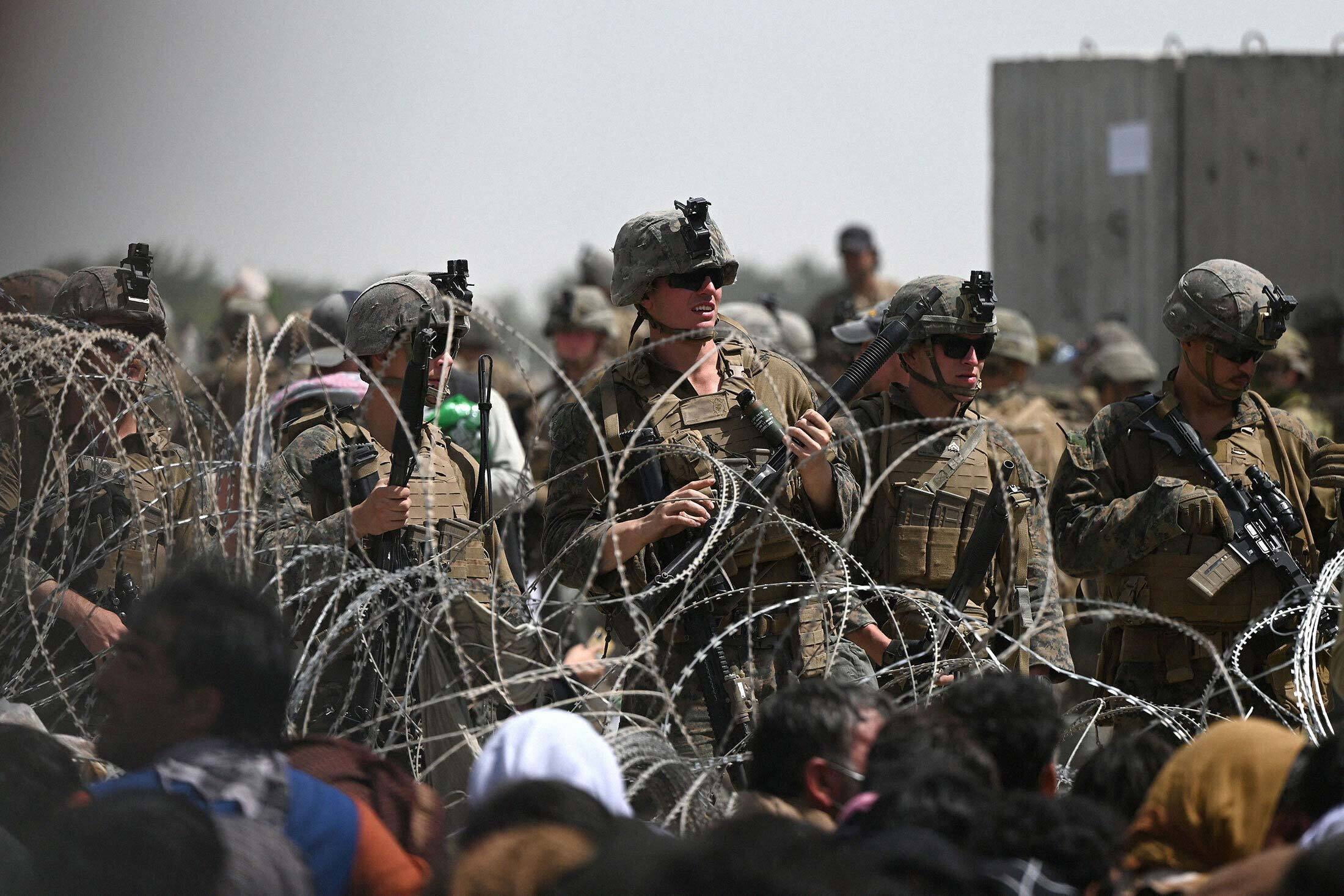 U.S. soldiers stand guard behind barbed wire as Afghans hoping to flee the country sit on a roadside near the military part of the airport in Kabul on Aug. 20.