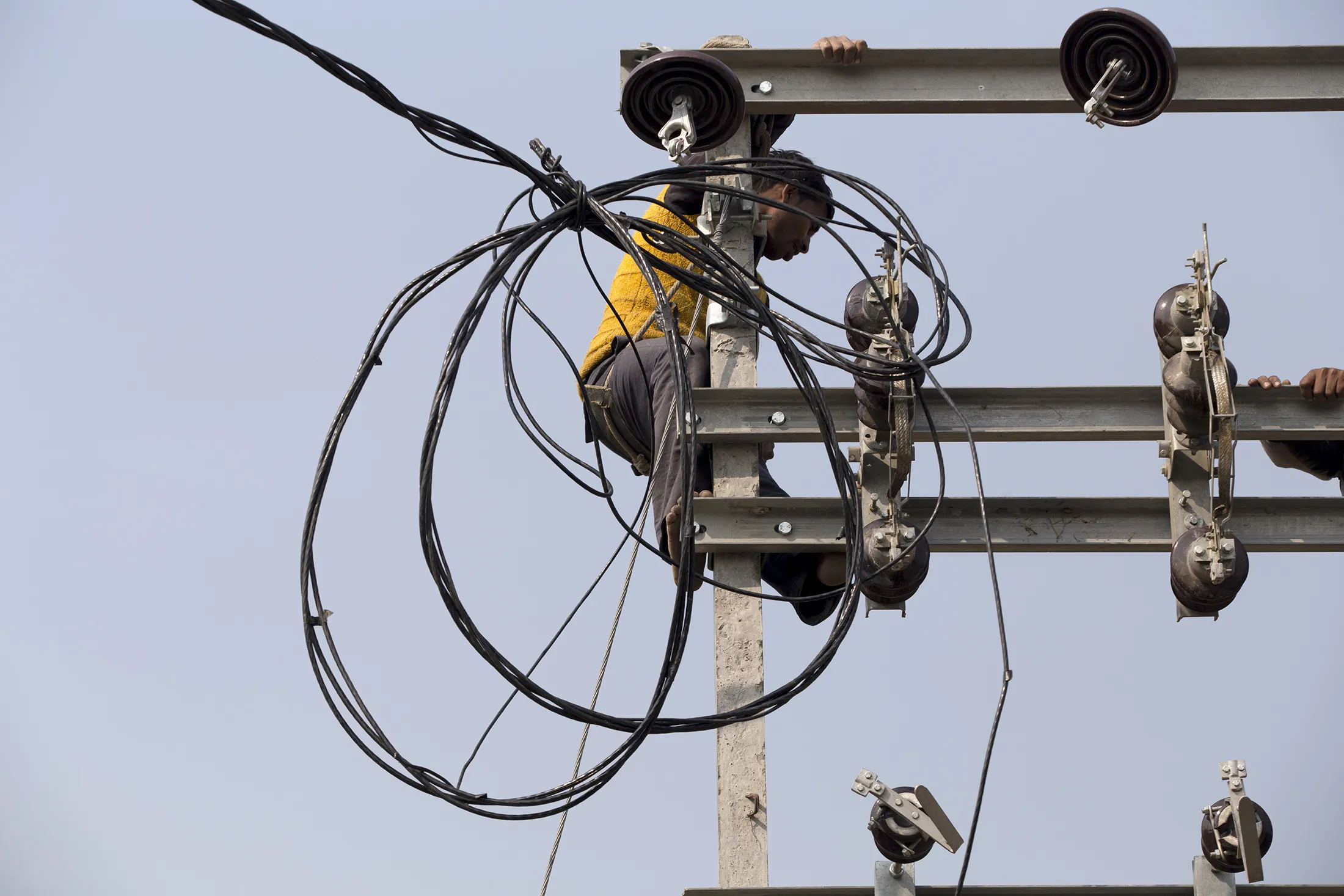 A worker stands on a transmission pole during an implementation program by the Rural Electrification Corp. in the village of Manpur Kulchaura, Uttar Pradesh, India, on Jan. 15, 2017.
