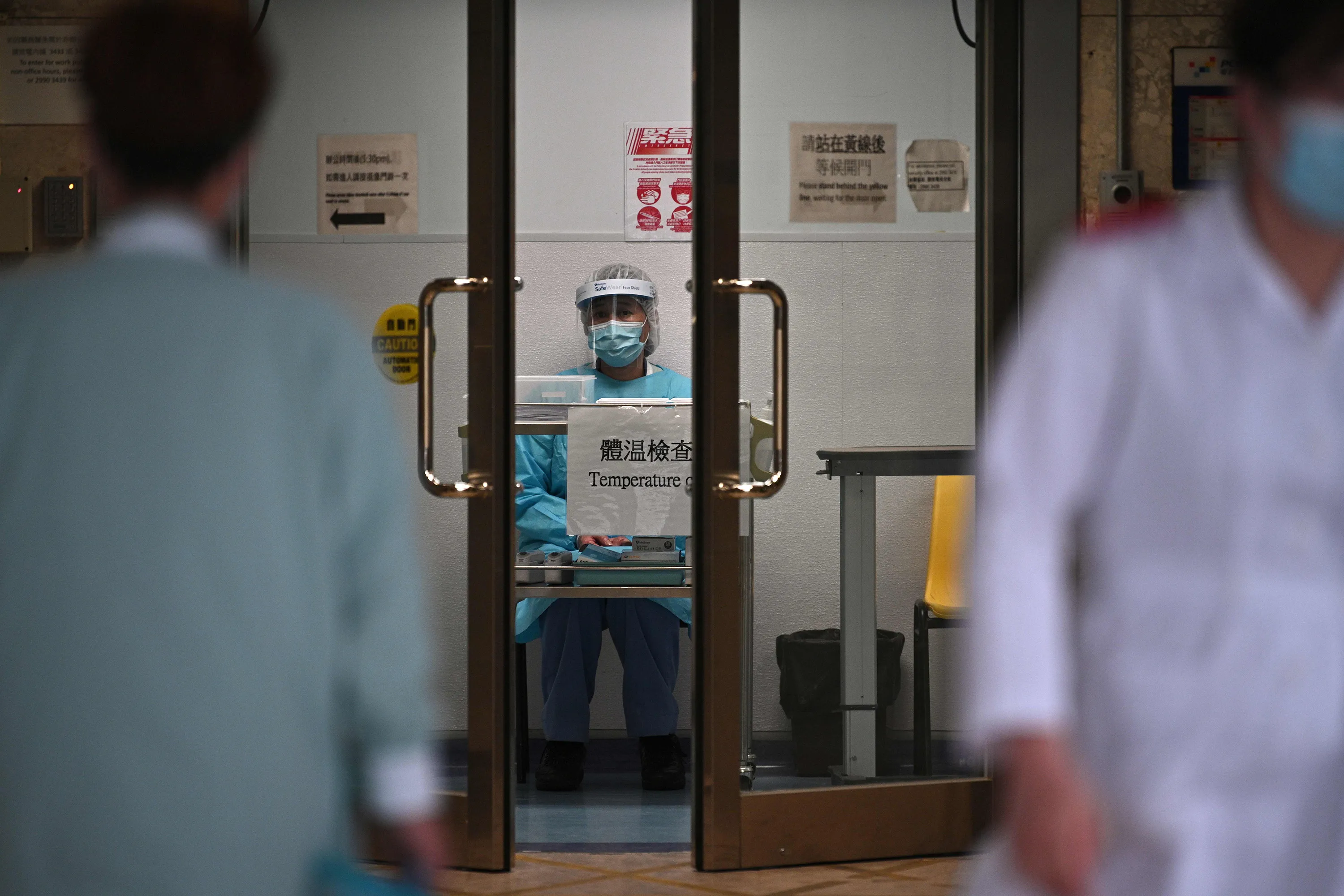 A medical worker wearing protective gear waits to take the temperature of people in an entrance of a hospital in Hong Kong.