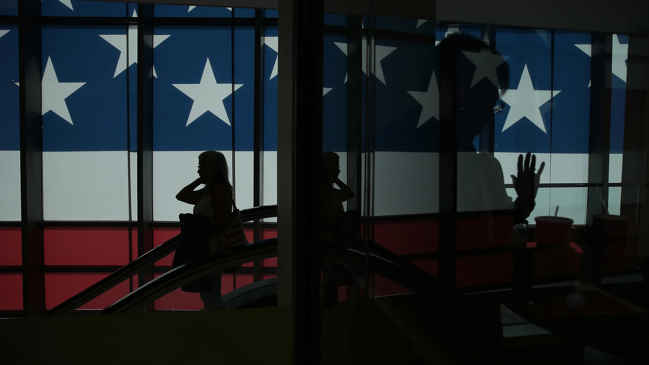 The silhouette of a delegate is seen in front of a window covered in an American flag decal during the Republican National Convention (RNC) in Cleveland, Ohio, U.S., on Monday, July 18, 2016. The day before the start of the Republican National Convention in Cleveland, Reince Priebus said Donald Trump has to use the gathering to convince Americans he can be presidential.

