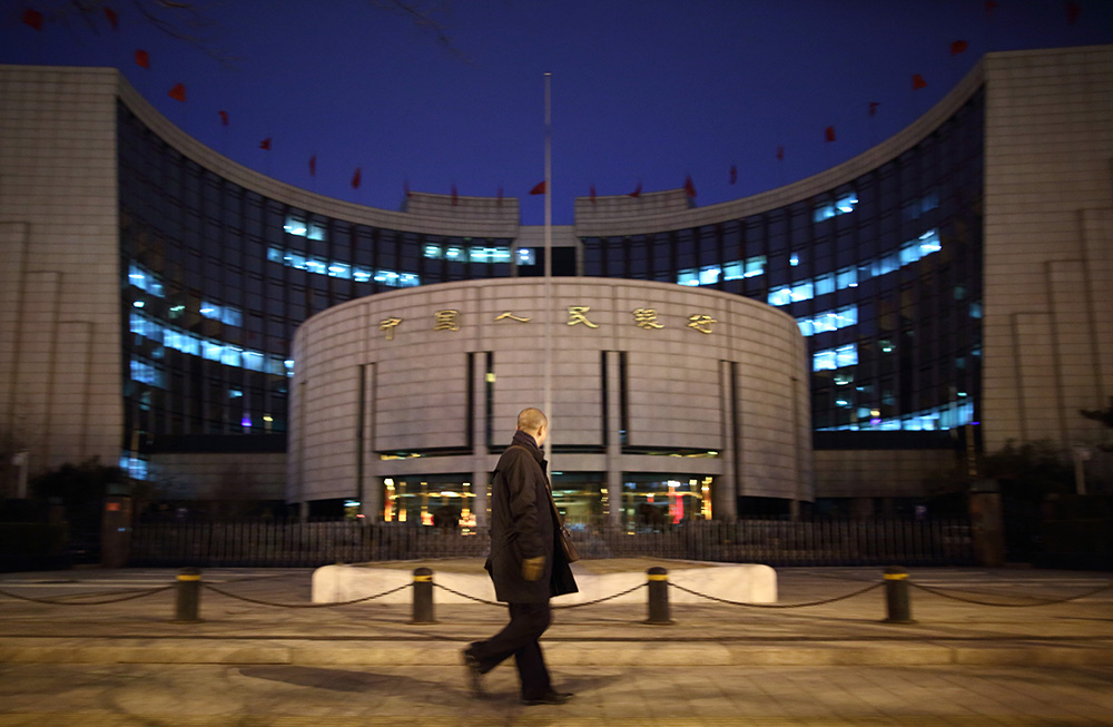 A pedestrian walks past the People's Bank Of China (PBOC) headquarters at night in the financial district of Beijing, China.
