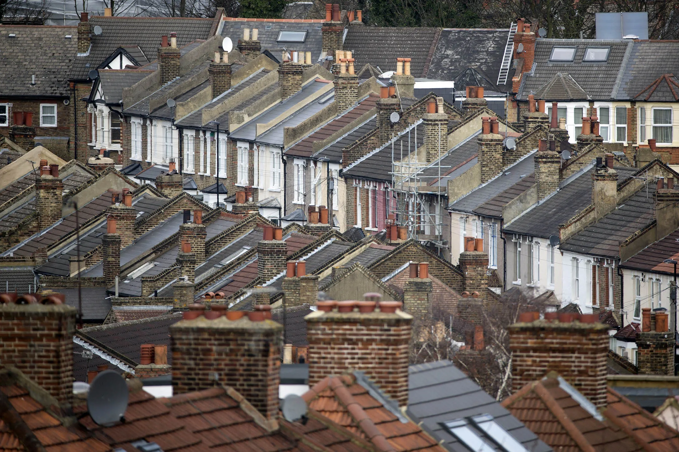 Brick chimney stacks stand on the tiled rooftops of houses on a residential street in London, U.K.