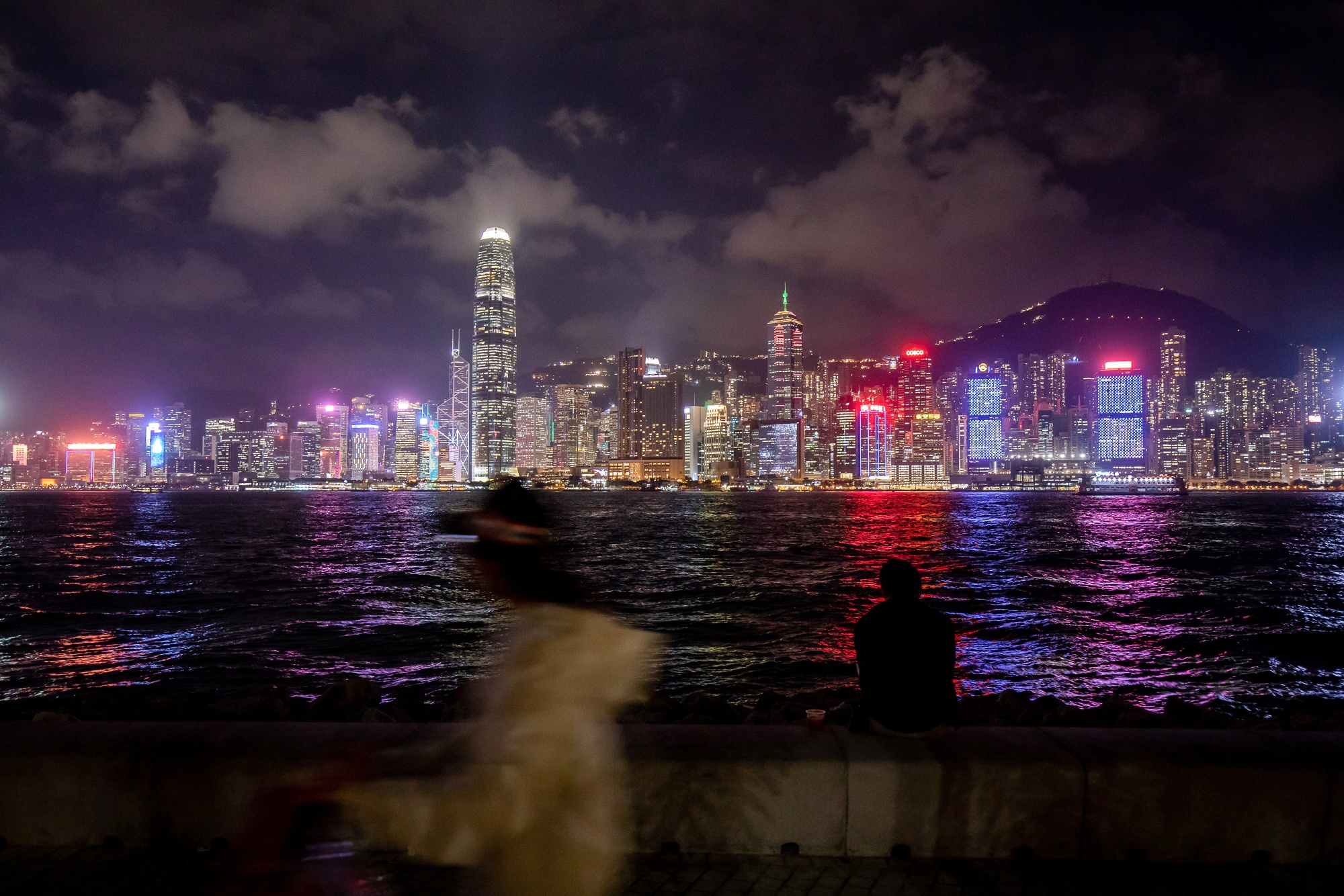 A pedestrian walks along a promenade in front of the city's skyline in Hong Kong, China.