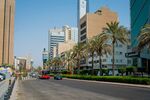 A bus and an automobile drive along an empty road past commercial office buildings in Kuwait City, Kuwait.