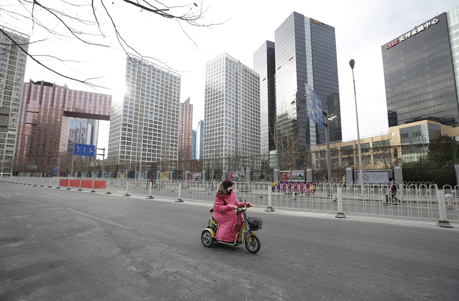 A woman drives a motorbike past office buildings in Beijing's central business district on the eve of the Chinese Lunar New Year, in Beijing, China, February 7, 2016.