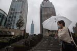 A pedestrian holding an umbrella walks past the Taipei 101 building, center, and other commercial buildings in Taipei, Taiwan.