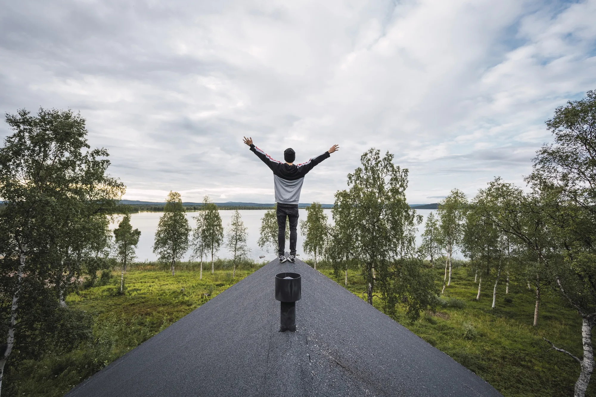Finland, Lapland, man standing on roof of a house at a lake with raised arms