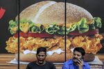 Men sit in front of an advertisement for a menu item outside a Burger King restaurant in Mumbai.