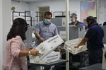 Workers wearing protective masks carry U.S Postal Service bins with mail-in ballots in Miami.&nbsp;