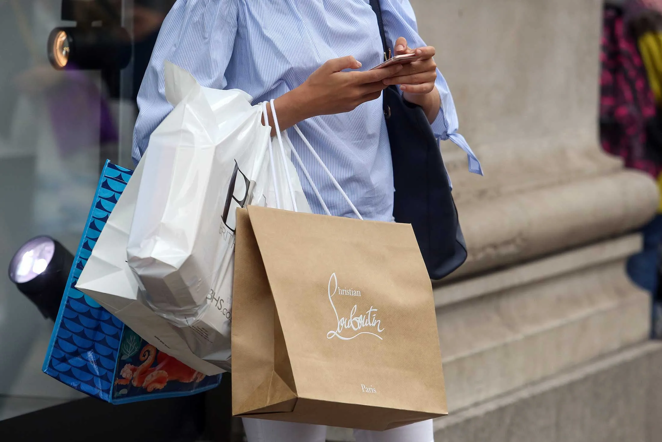 A shopper checks her mobile phone while holding shopping bags on Oxford Street in London, U.K.
