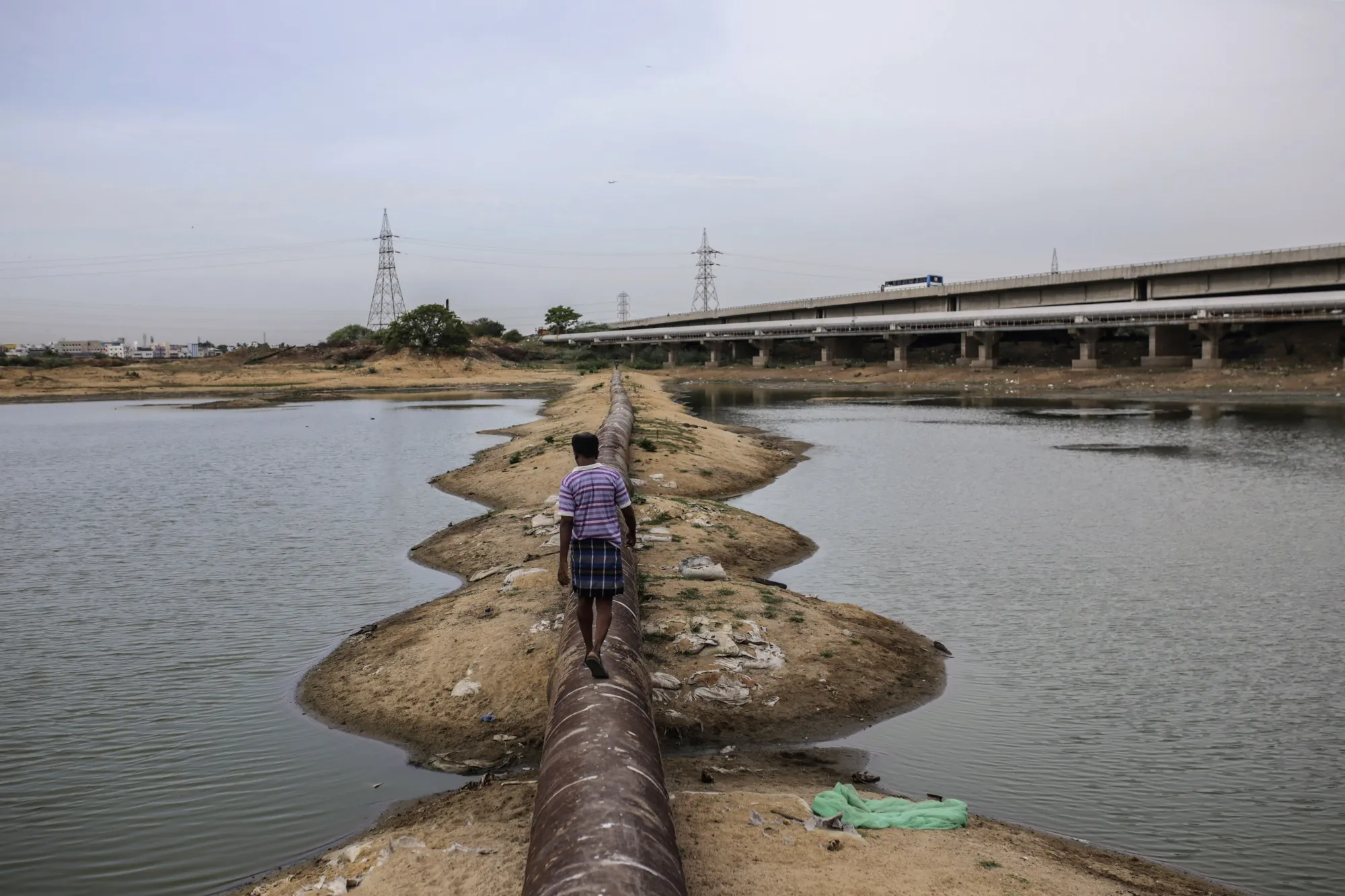 A man walks along a water pipe on the bottom of&nbsp;Porur Lake in Chennai, India.