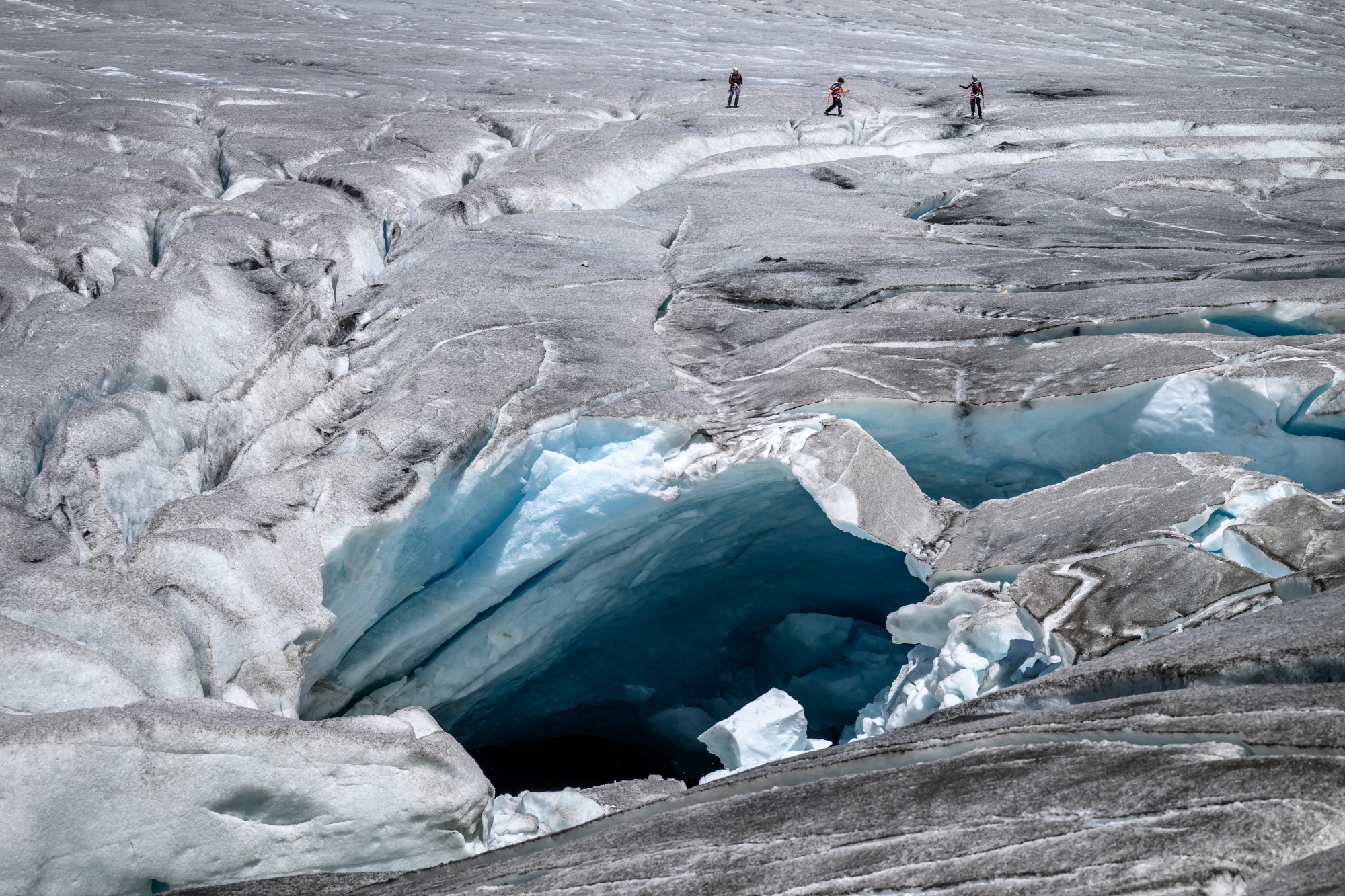 A group of hikers make their way past a melt hole on Rhone Glacier in the Swiss Alps, in July.