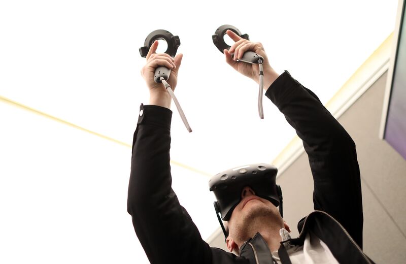 An attendee holds virtual control sticks whilst wearing a HTC Corp. Vive virtual reality (VR) headset at the Virtual Reality World Congress in Bristol, U.K., on Wednesday, April 12, 2017. Virtual reality proponents say that liberating computing from the confines of glass rectangles will change the way people interact with information. Photographer: Chris Ratcliffe/Bloomberg