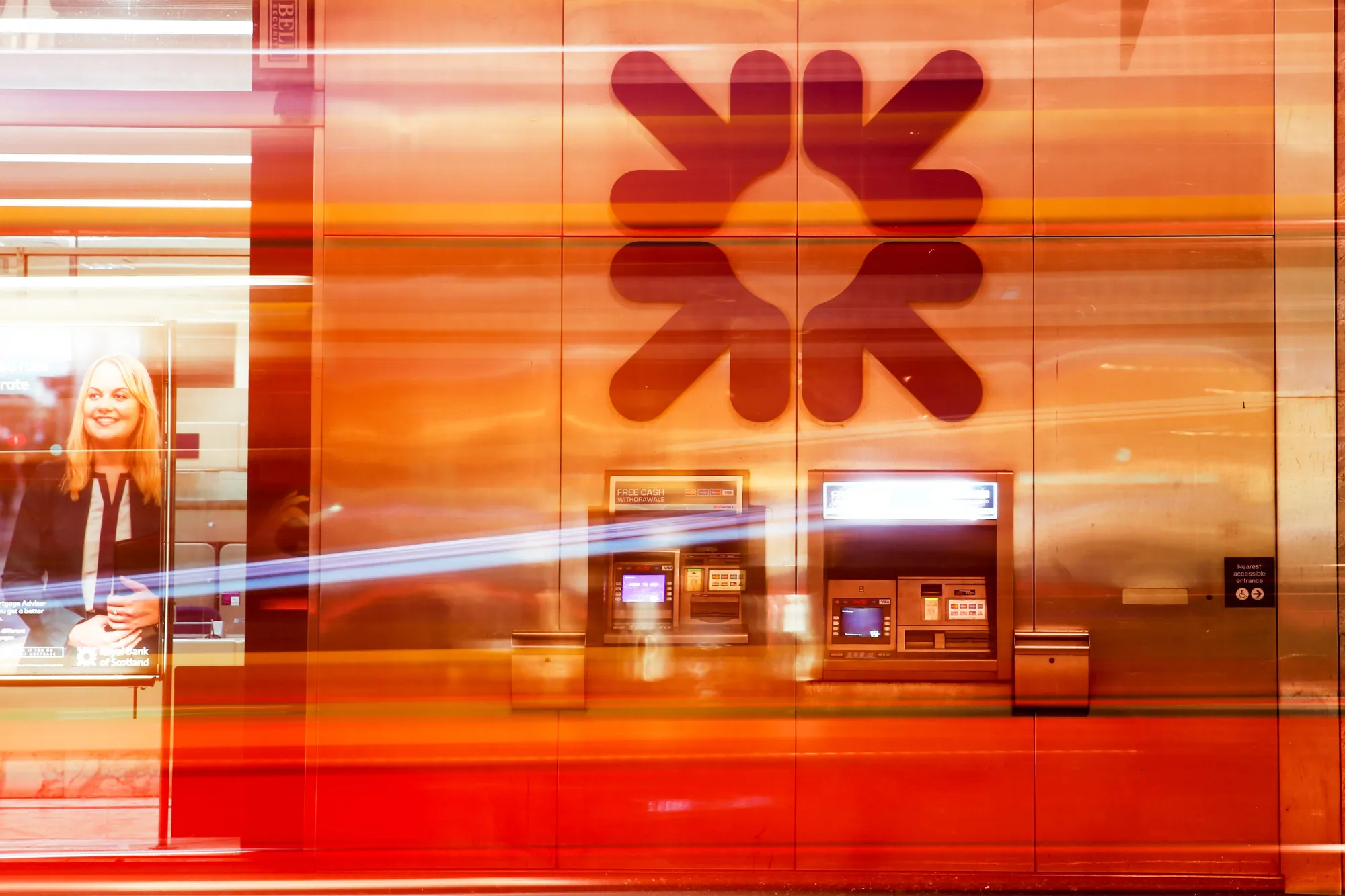 Traffic leaves light trails while passing a Royal Bank of Scotland Group Plc bank branch in London, U.K., on Wednesday, Feb. 15, 2017. RBS is preparing to cut more than 1 billion pounds ($1.25 billion) of annual operating costs by eliminating jobs and closing branches as it seeks to bolster profitability, said a person with knowledge of the plans.
