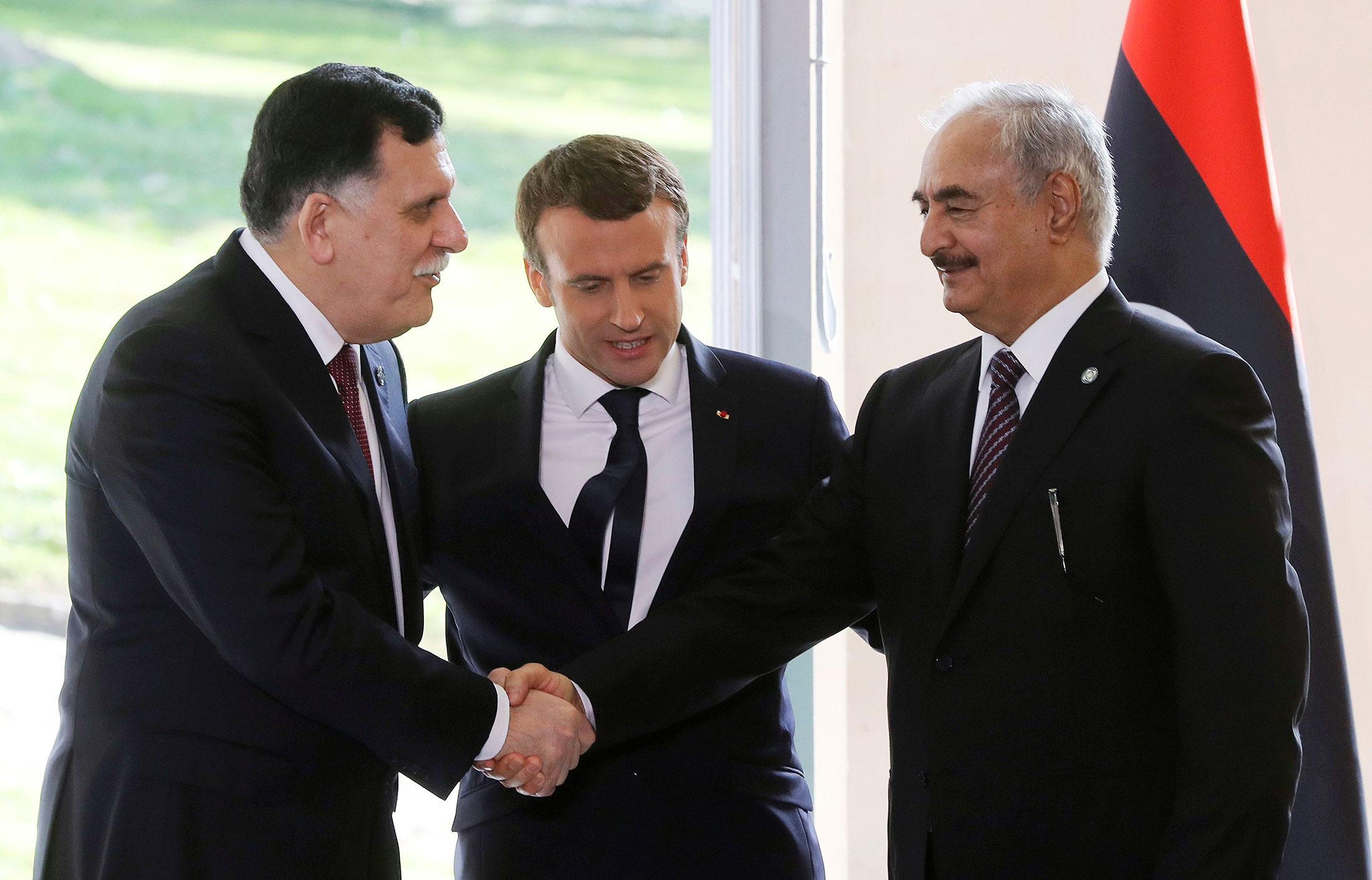 Emmanuel Macron looks on as Fayez al-Sarraj shakes hands with General Khalifa Haftar after talks aimed at easing tensions in Libya, in La Celle-Saint-Cloud, near Paris, on July 25, 2017.
