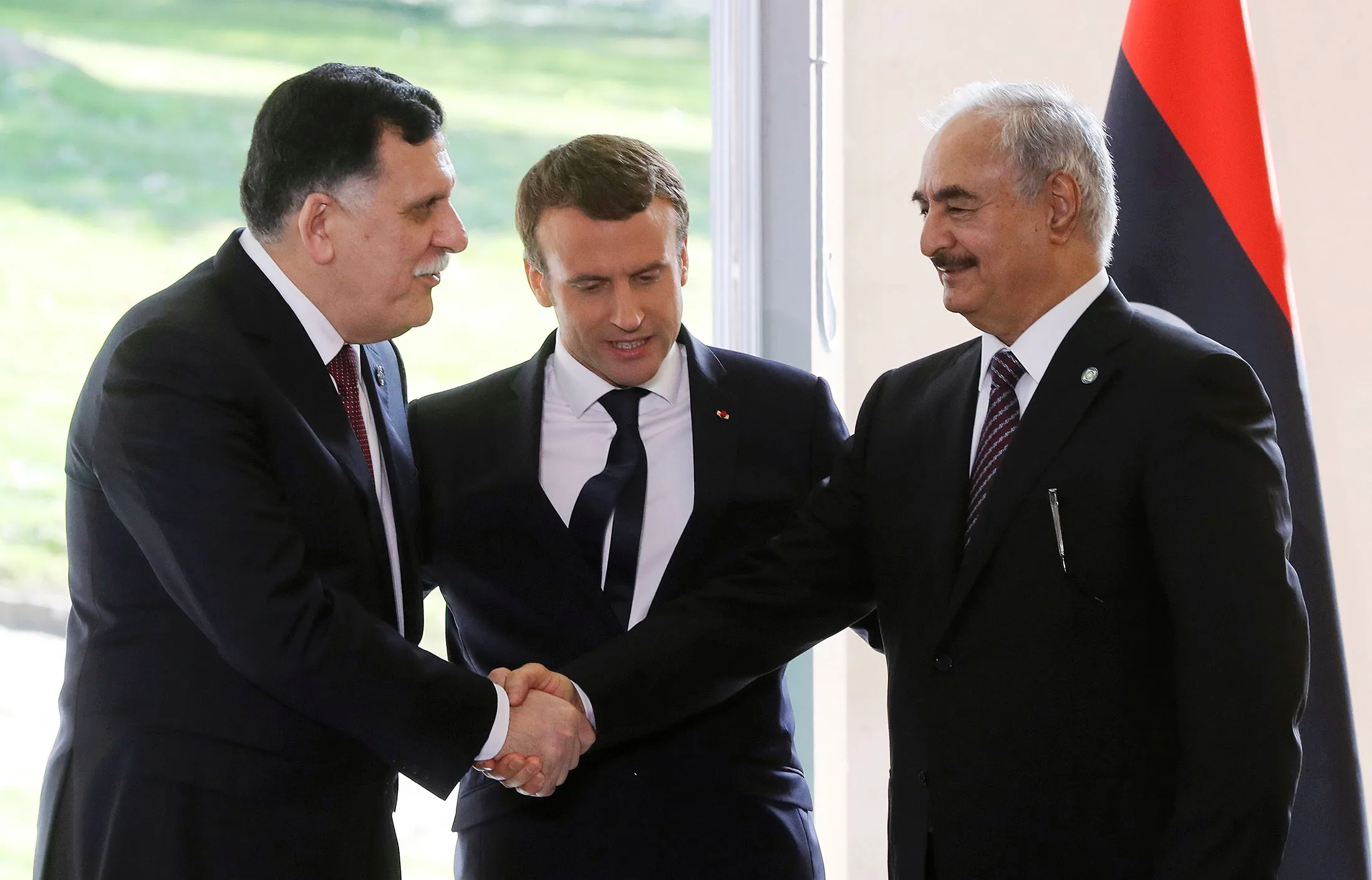 Emmanuel Macron looks on as Fayez al-Sarraj shakes hands with General Khalifa Haftar after talks aimed at easing tensions in Libya, in La Celle-Saint-Cloud, near Paris, on July 25, 2017.
