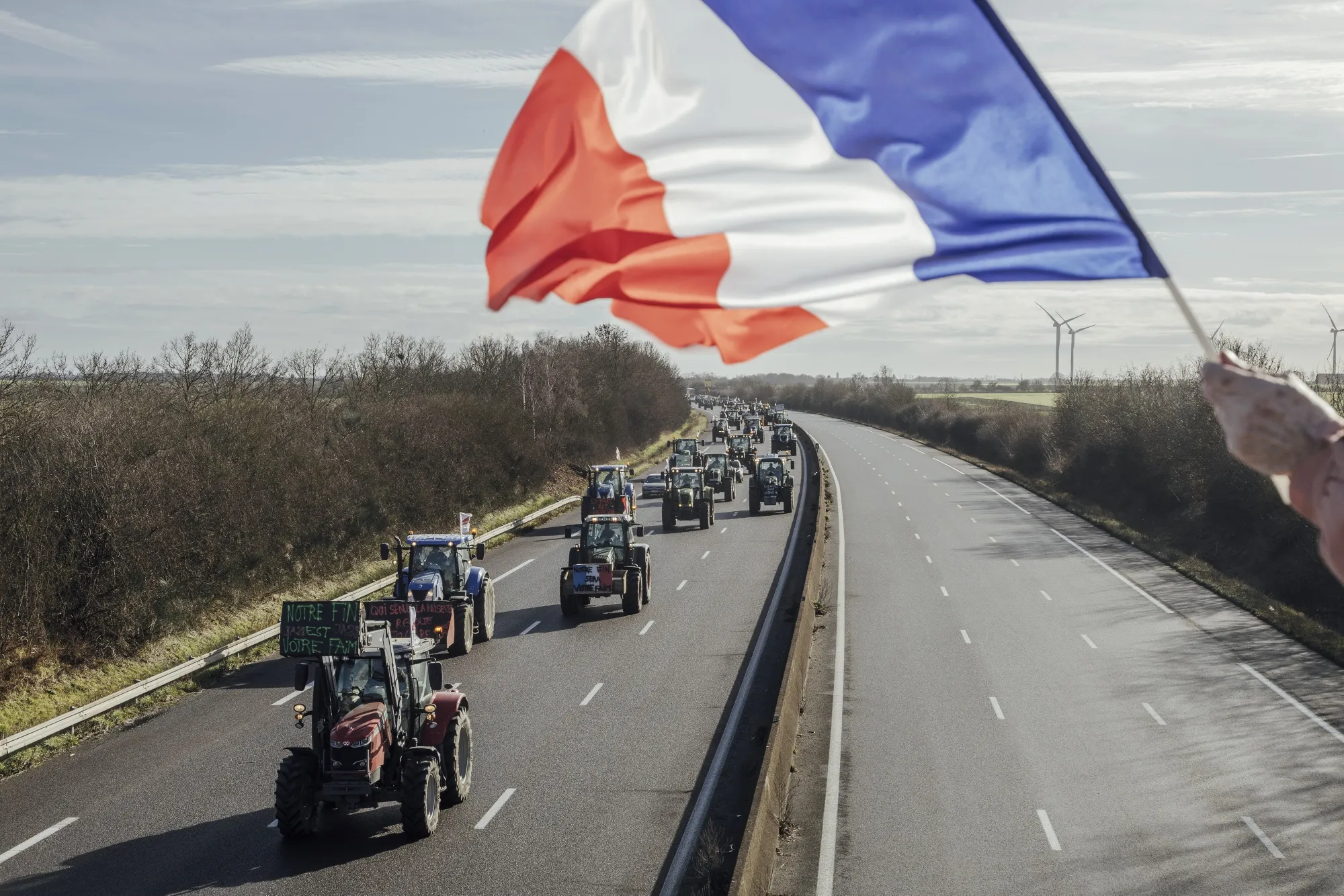 A supporter waves a French flag as a convoy of farmers drive tractors along the A10 highway en route to blockade the toll road barriers at Saint Arnoult-en-Yvelines, at Allainville, France, on Friday.