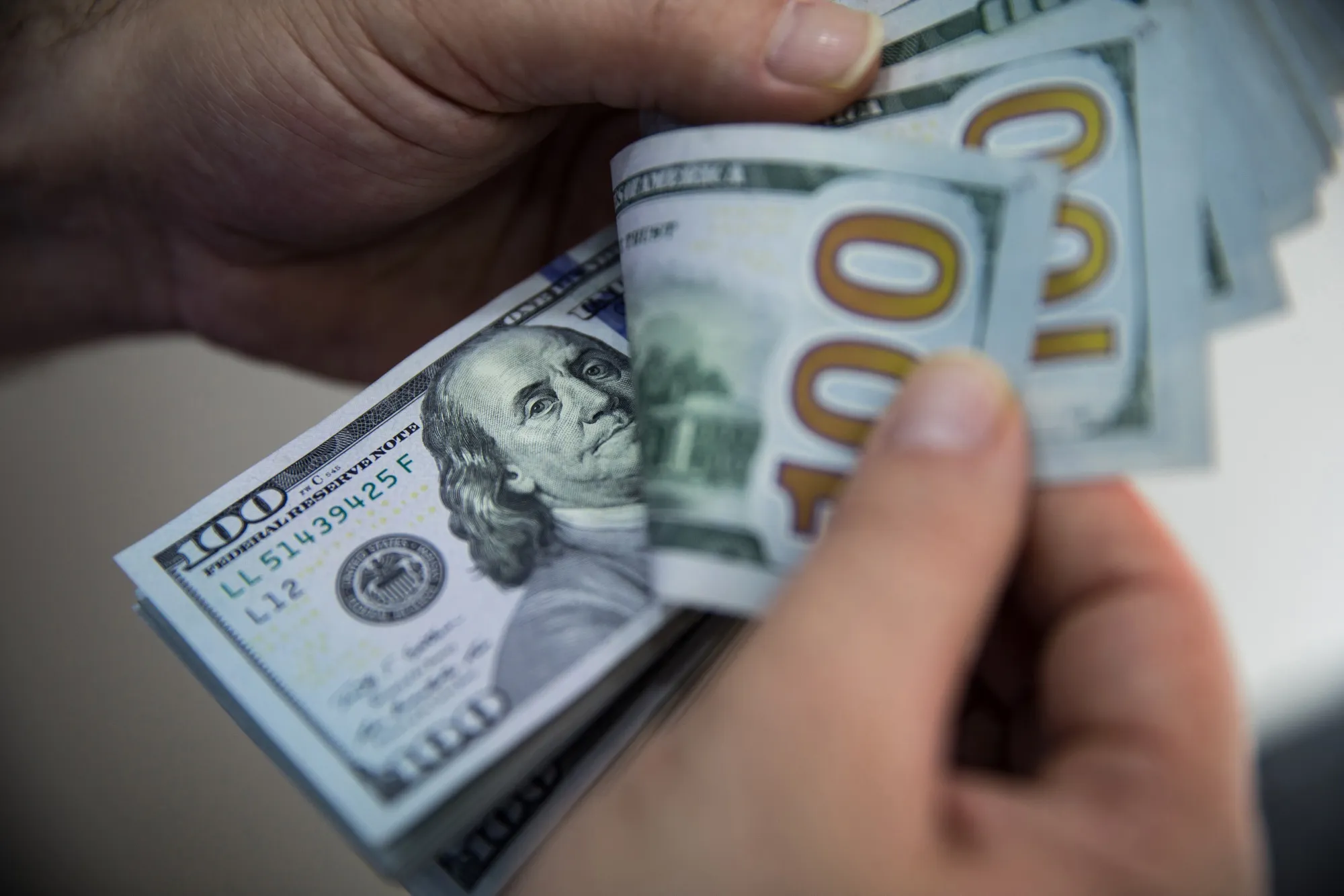 A customer counts 100 U.S. dollar banknotes.&nbsp;