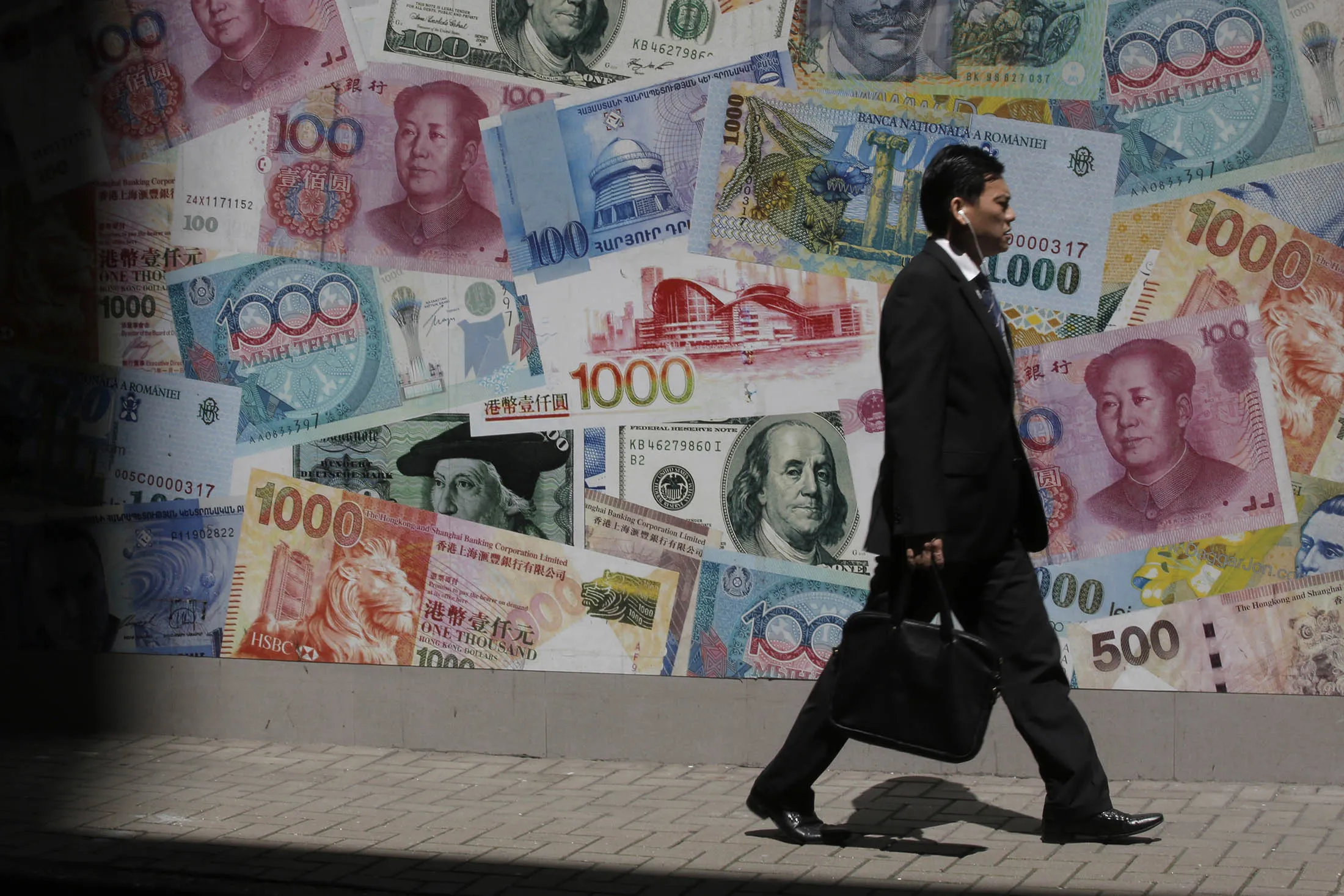 A man walks past a poster showing different countries bank notes in Hong Kong, Friday, June 24, 2016. The British pound is experiencing volatile trading as results from Britain’s vote on European Union membership is tallied.
