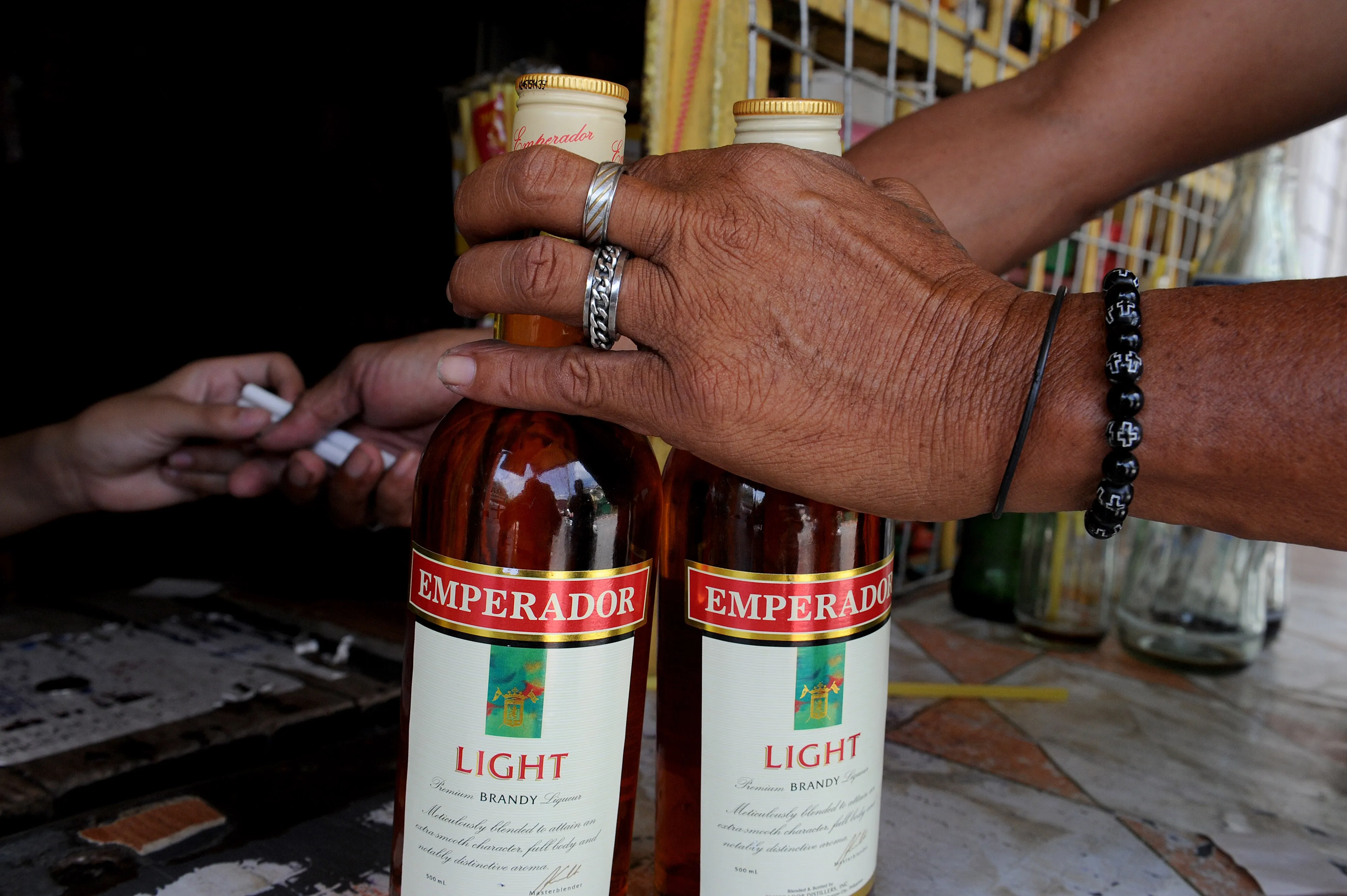 A customer buys bottles of Emperador brandy from a convenience store in suburban Manila.