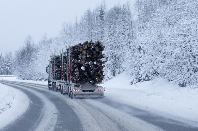 A truck transporting logs travels along a road cutting through forest in Sundsvall.
