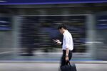 A pedestrian using his smartphone walks past an electronic stock board outside a securities firm in Tokyo, Japan.