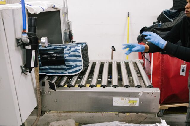 A worker places a reusable package through a sanitizing machine.