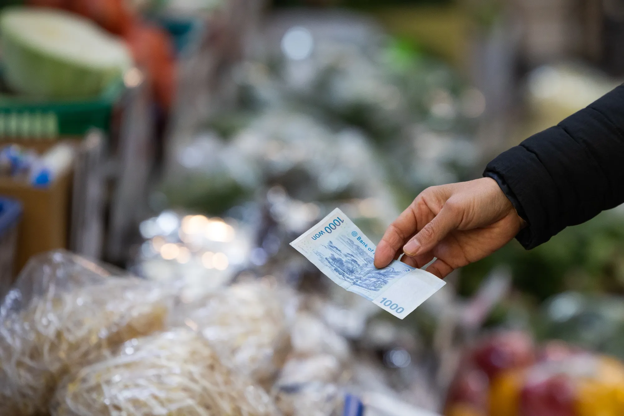 A customer holds a South Korean 1,000 Won banknote at a vegetable stall in Mangwon Market in Seoul.