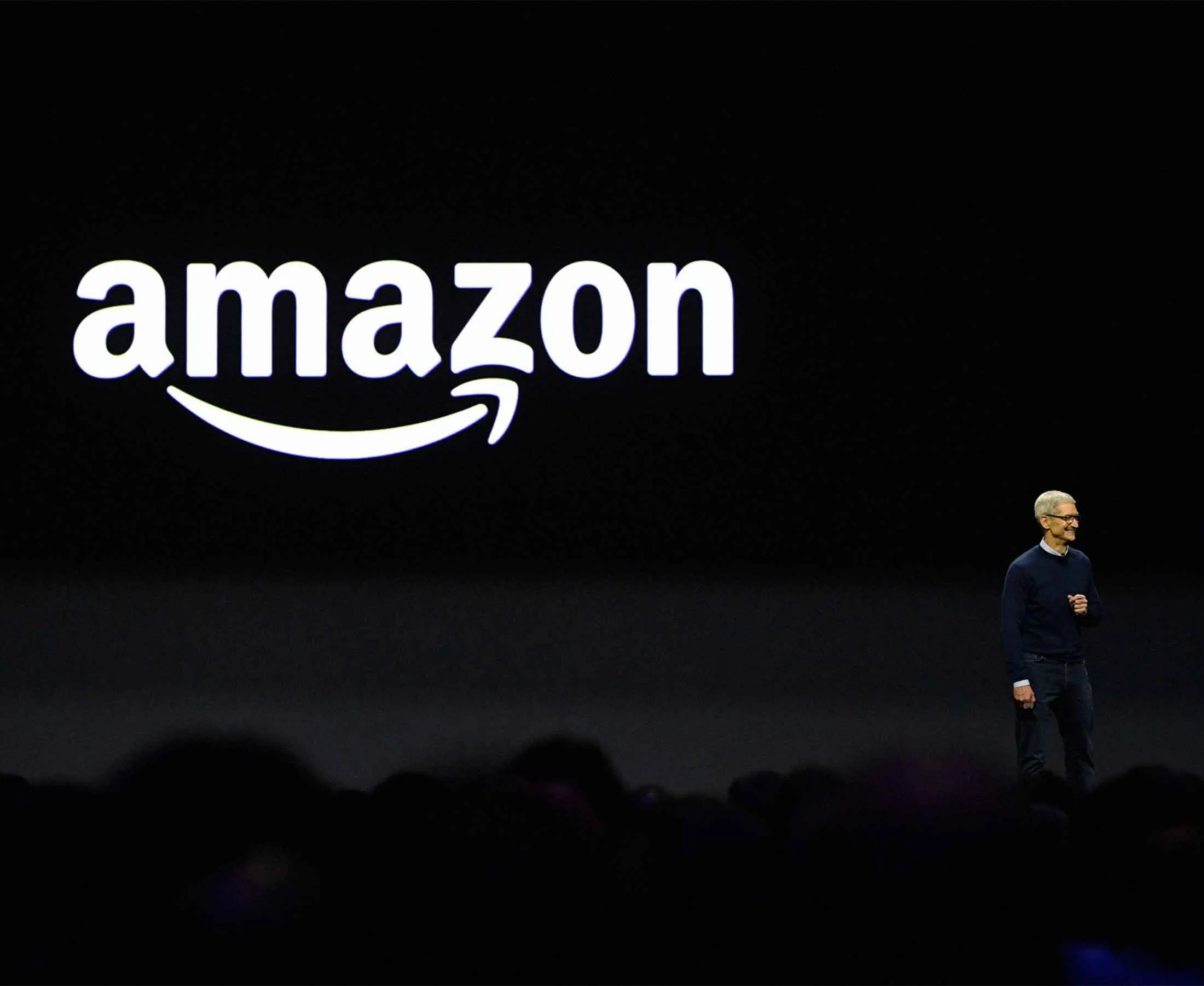 Tim Cook, chief executive officer of Apple Inc., smiles in front of a monitor displaying Amazon.com Inc. signage during the Apple Worldwide Developers Conference (WWDC) in San Jose, California, U.S., on Monday, June 5, 2017.&nbsp;
