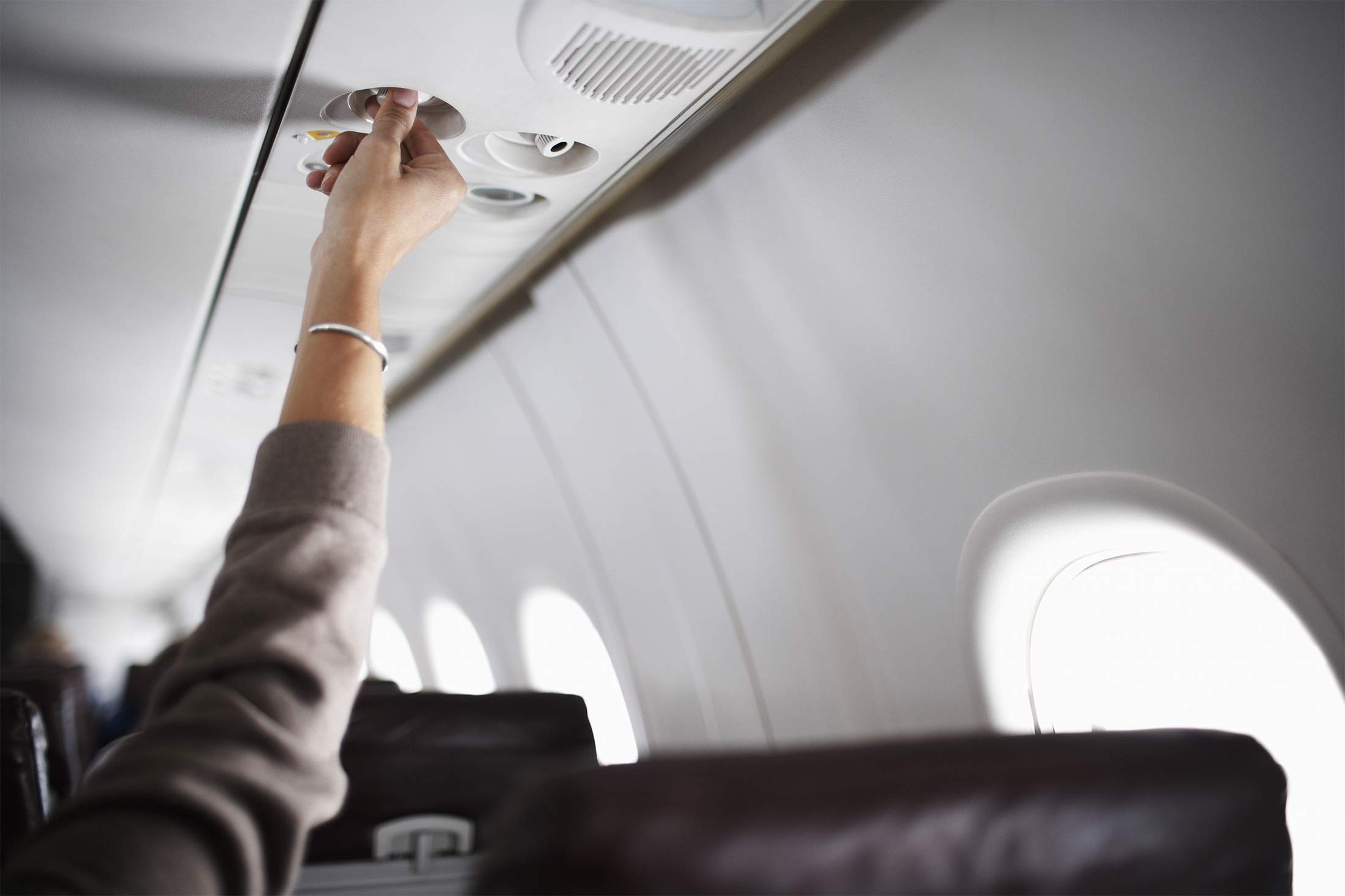 Woman reaching for air vent in airplane