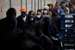 Shoppers wear protective masks while waiting in line behind a barrier of wooden pallets at a Costco Wholesale Corp. location in Hawthorne, California, U.S.