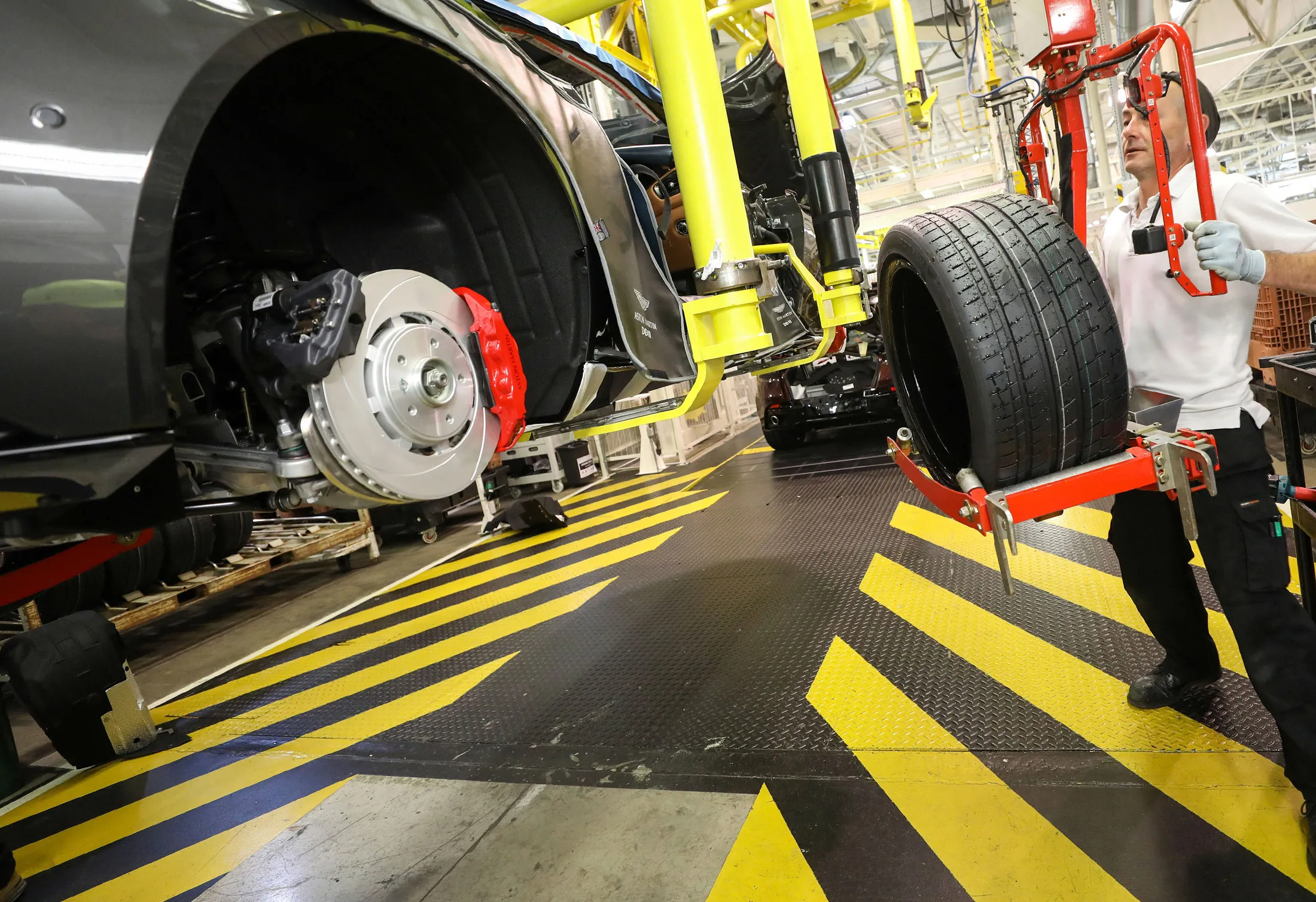 An employee prepares to fit a wheel to the rear of an Aston Martin DB11 luxury automobile on the final assembly line at Aston Martin Lagonda Ltd.'s manufacturing and assembly plant in Gaydon, U.K., on Tuesday, June 6, 2017. Aston Martin may consider an initial public offering as early as next year as the British maker of James Bond’s cars seeks to capitalize on the success of Ferrari NV’s listing to lure investors, people familiar with the matter said.
