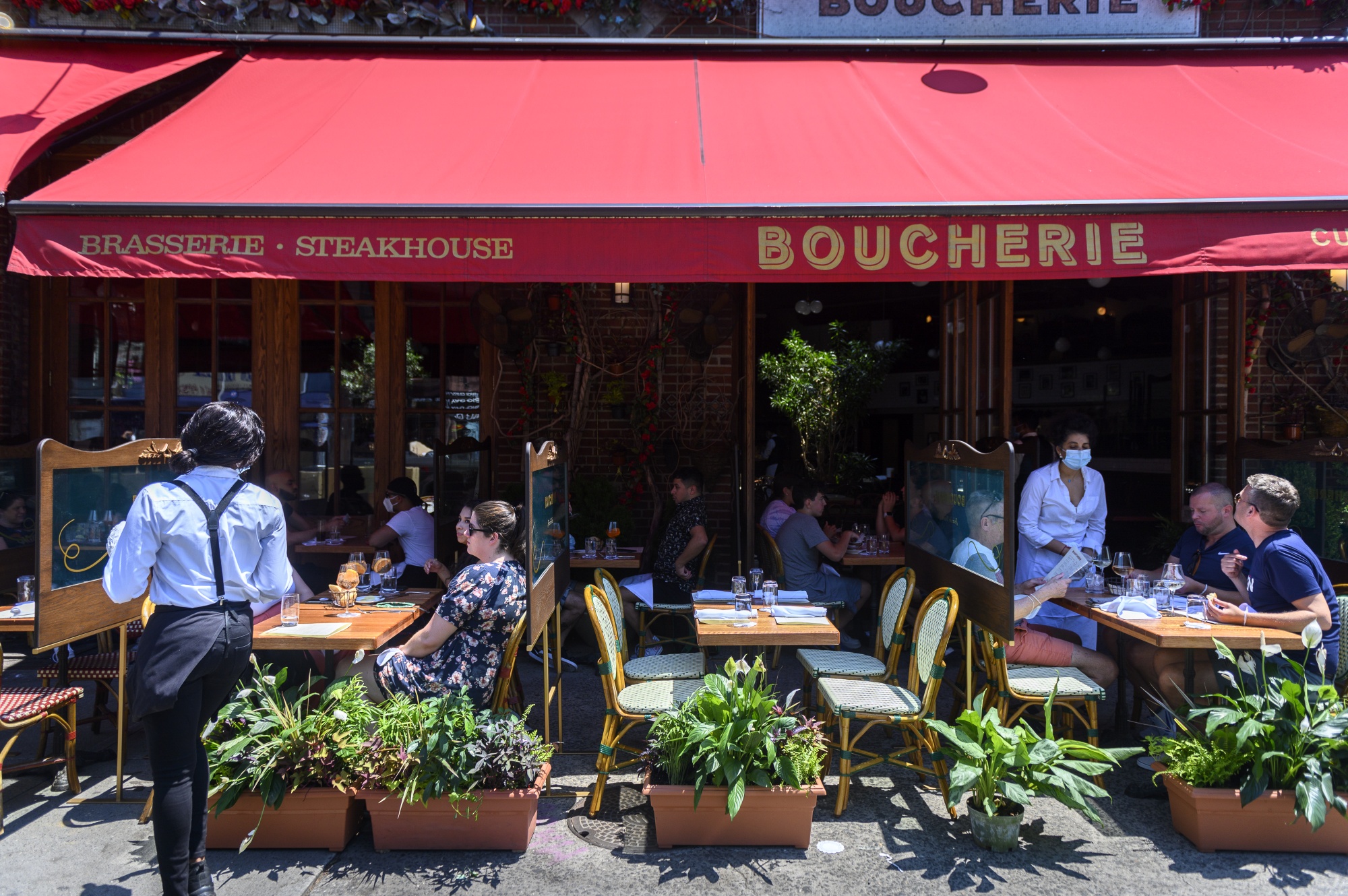 Servers wearing protective masks assist customers at tables outside of the Boucherie restaurant in the West Village neighborhood of New York.