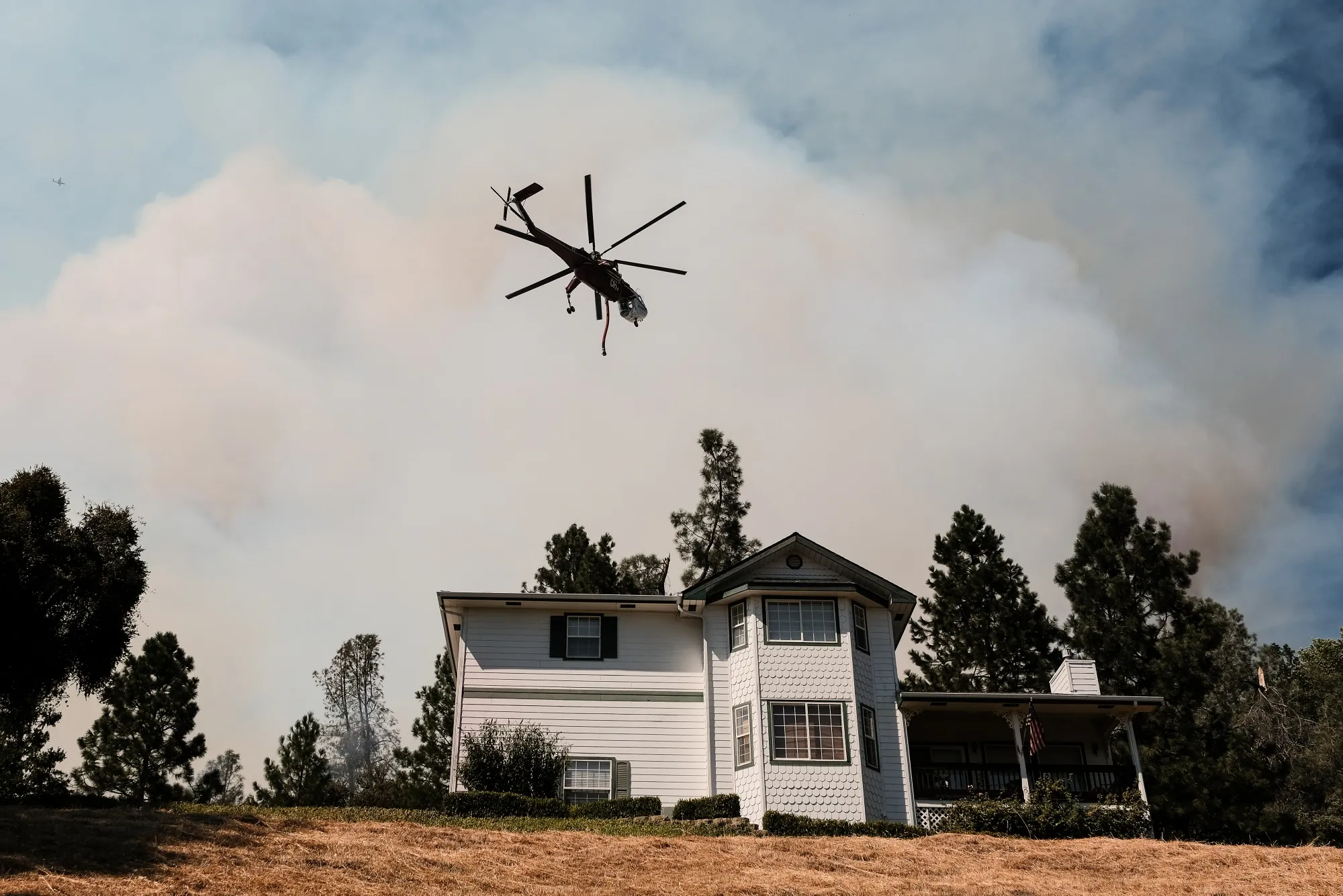 A helicopter flies over a fire near a home on Pinecrest Drive during the Oak Fire in Mariposa County, California, on July 23, 2022.&nbsp;