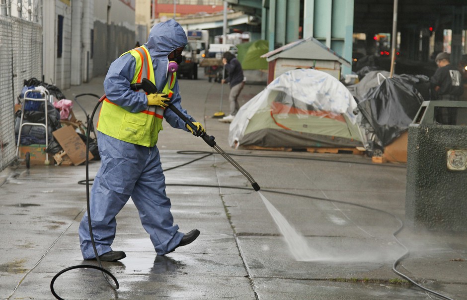 A city worker power-washes a sidewalk near a tent city in San Francisco in 2016.