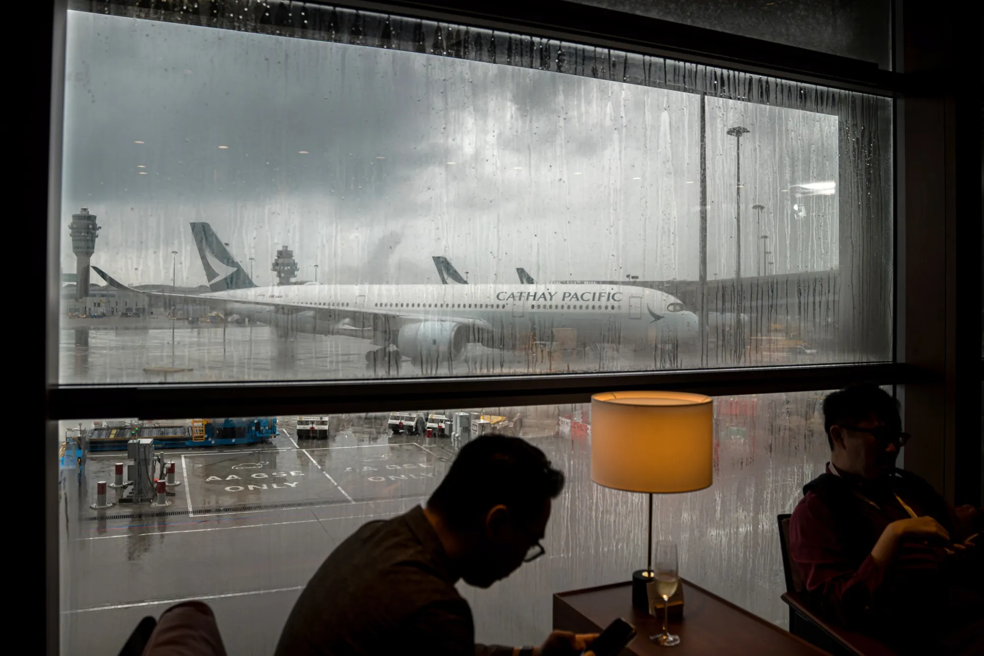 A Cathay Pacific Airways Ltd. aircraft on the tarmac beyond the company's The Bridge lounge at Hong Kong International Airport.