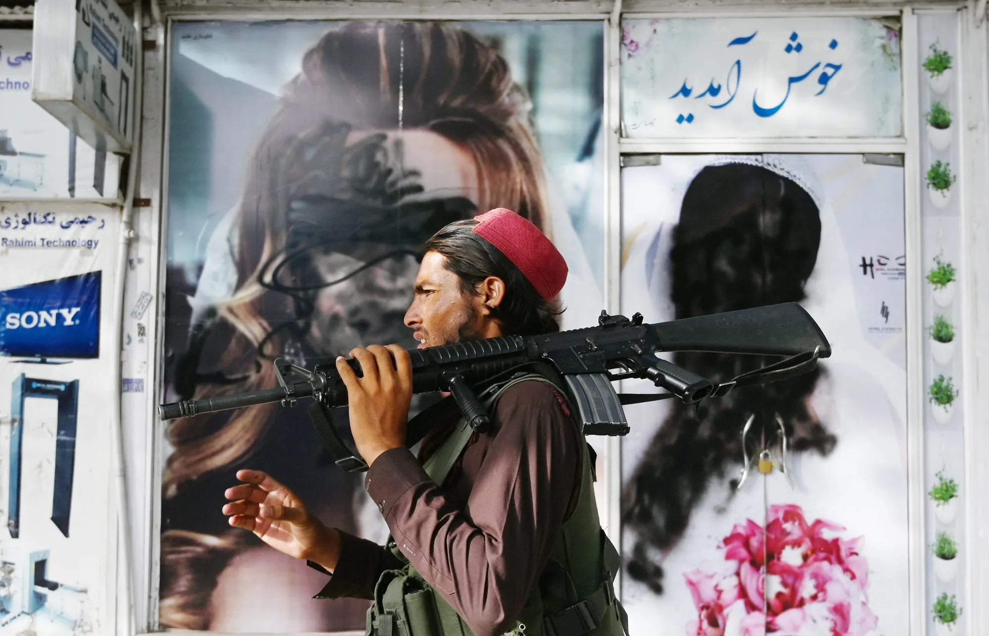 A Taliban fighter walks past a beauty salon with images&nbsp;defaced using spray paint, in Kabul in 2021.