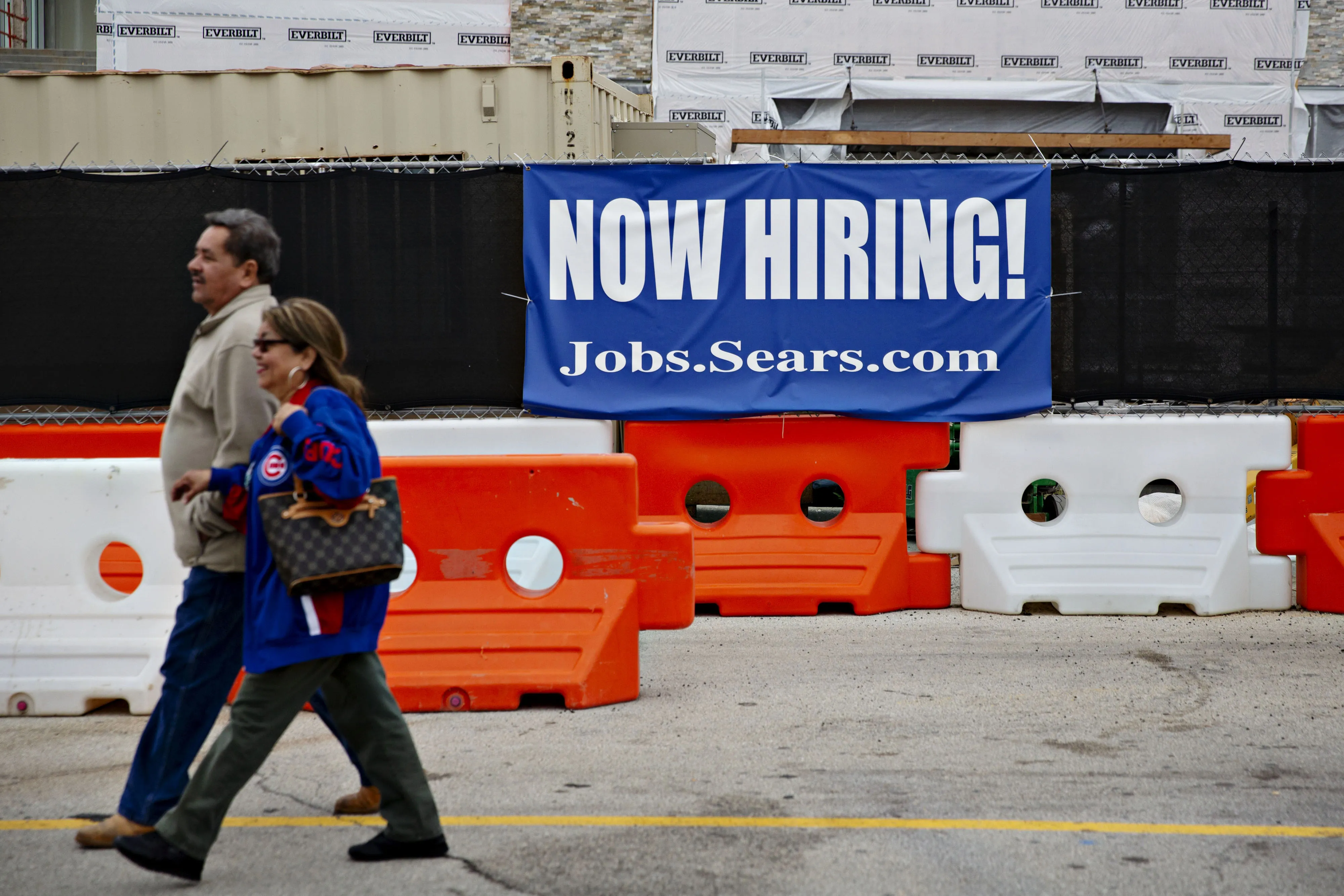 Shoppers walk by a "Now Hiring" sign.