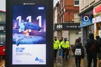 People walk past the NHS 111 publicity campaign poster in