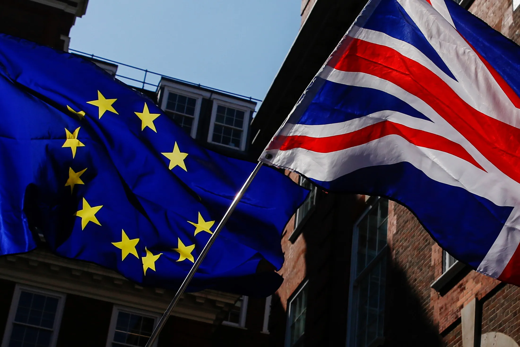 Campaigners wave an European Union (EU) flag and a Union flag, also known as a Union Jack, during an anti-Brexit demonstration outside the Conservative Party general-election campaign headquarters in London, U.K., on Friday, May 26, 2017. Brexit Secretary David Davis said European Union demands to protect its citizens' rights in the U.K. are "ridiculously high" and will be the first subject of negotiations to exit the bloc after next month’s election.
