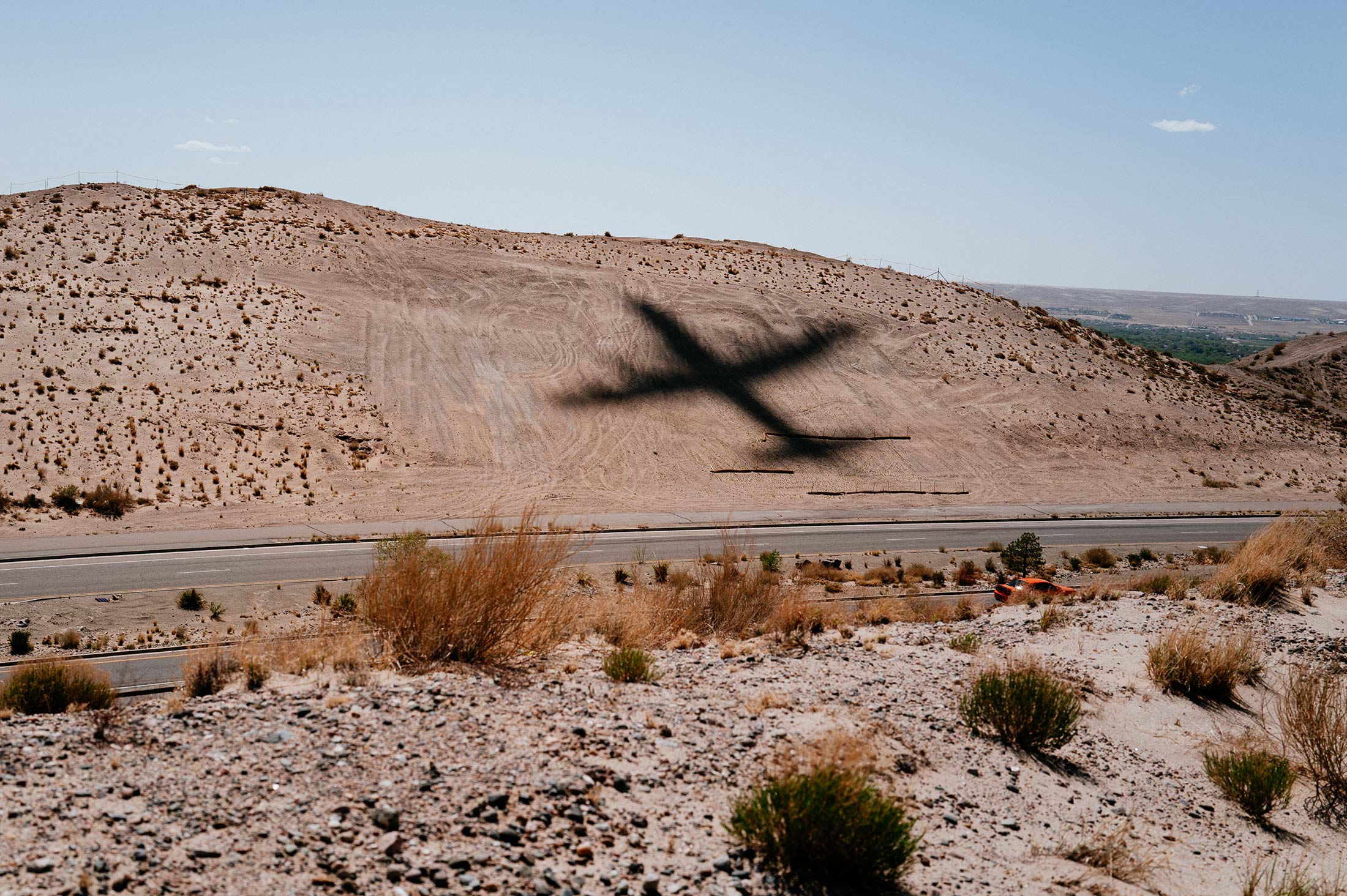 Shadow of a plane over a dry hillside near Albuquerque's airport, where ICE detainees are flown in before transfer to New Mexico detention centers.